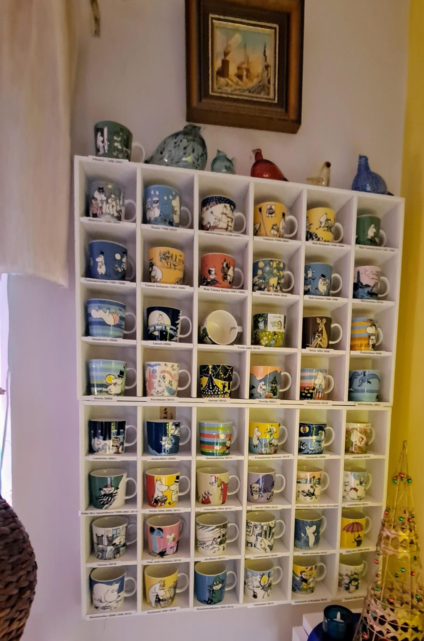 Moomin mugs with names, neatly arranged on the shelf in rows and stacked