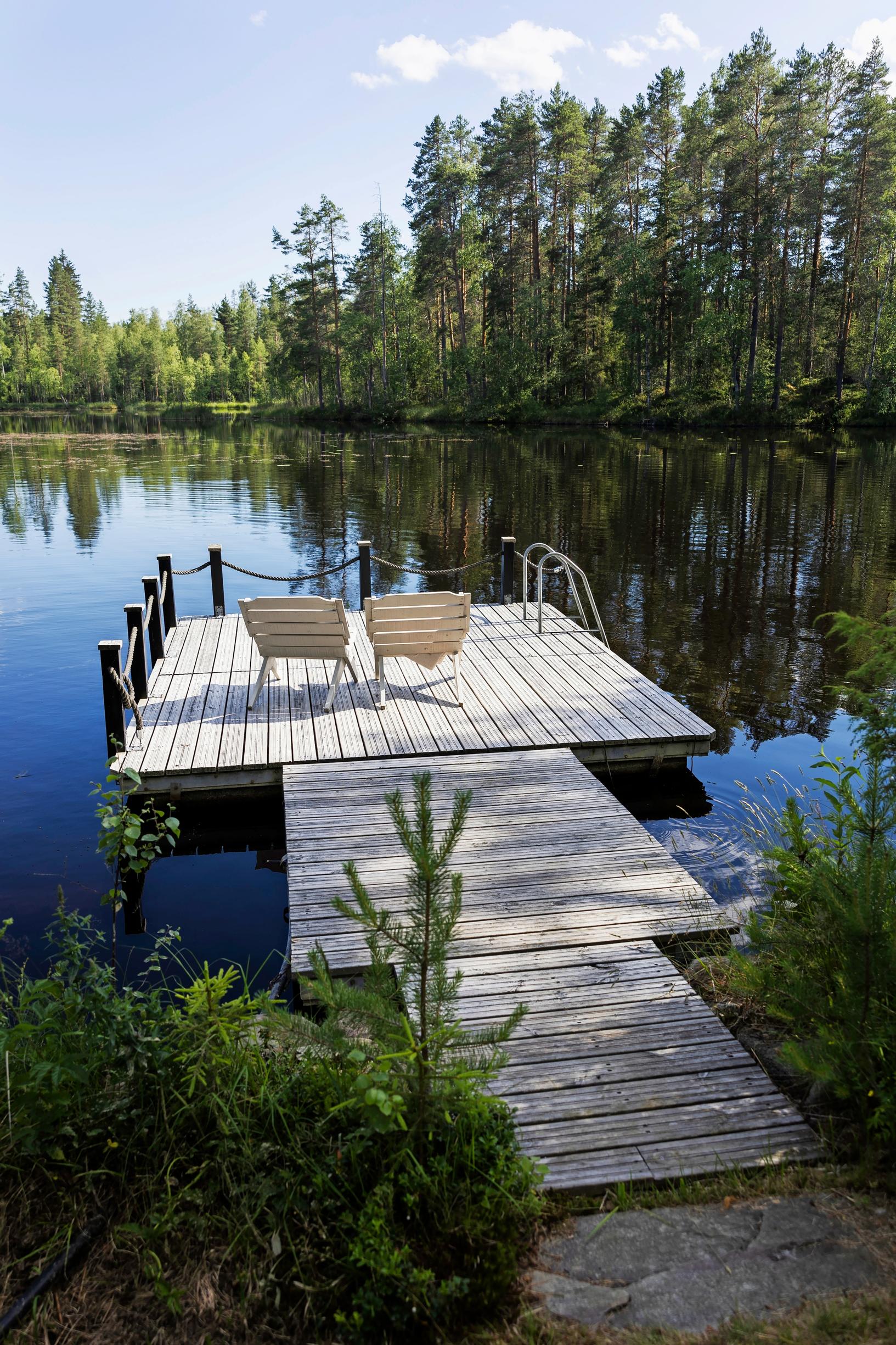 two lounge chairs on a dock, with a forested shoreline in the distance