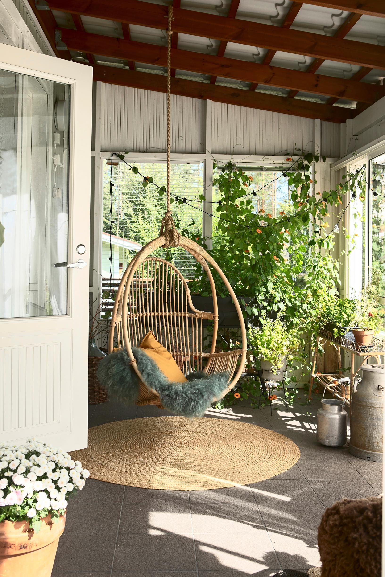 A rattan hanging chair and a round sisal rug in a single-family home’s greenhouse