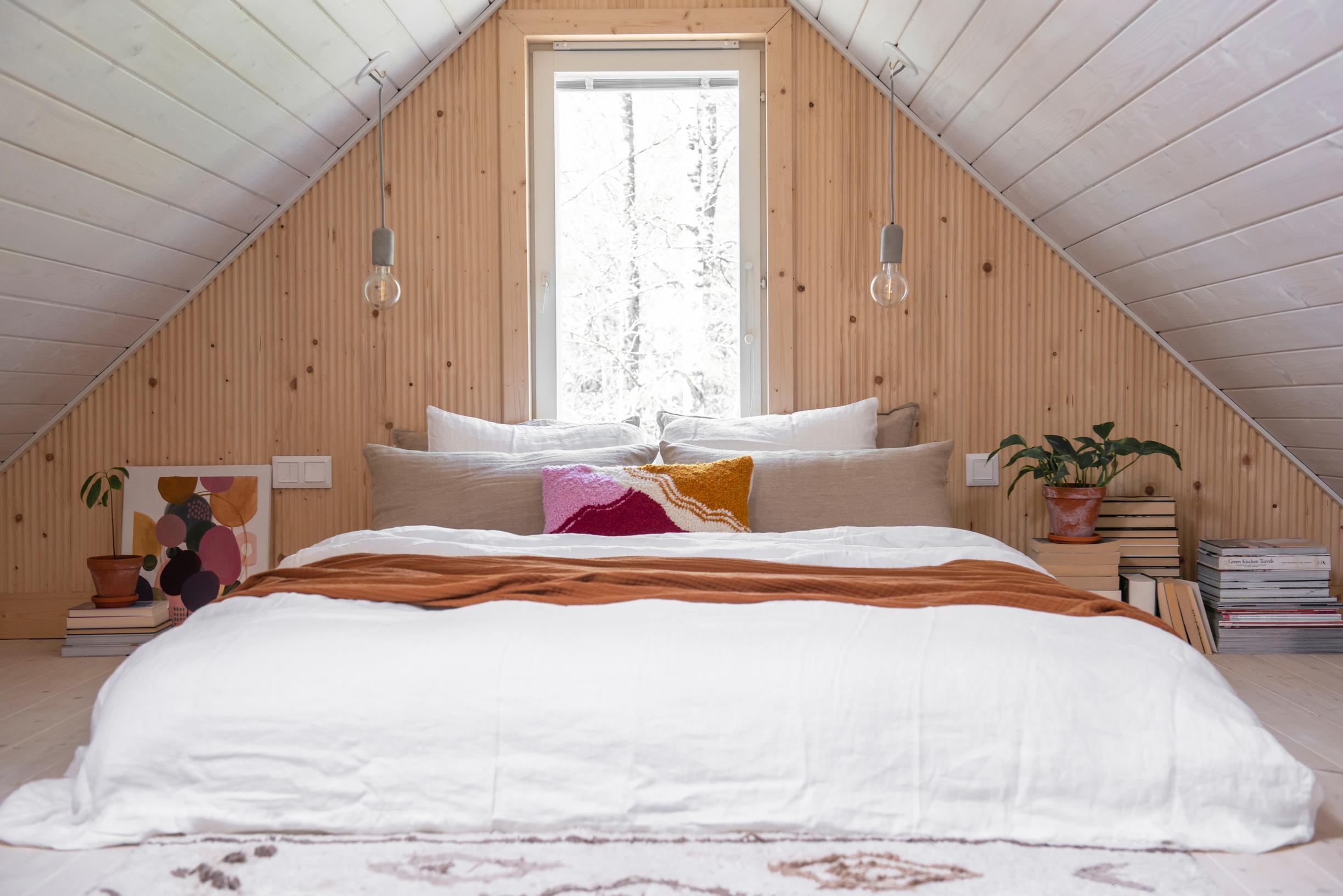 A wide bed in a gable-windowed bedroom under a sloping roof