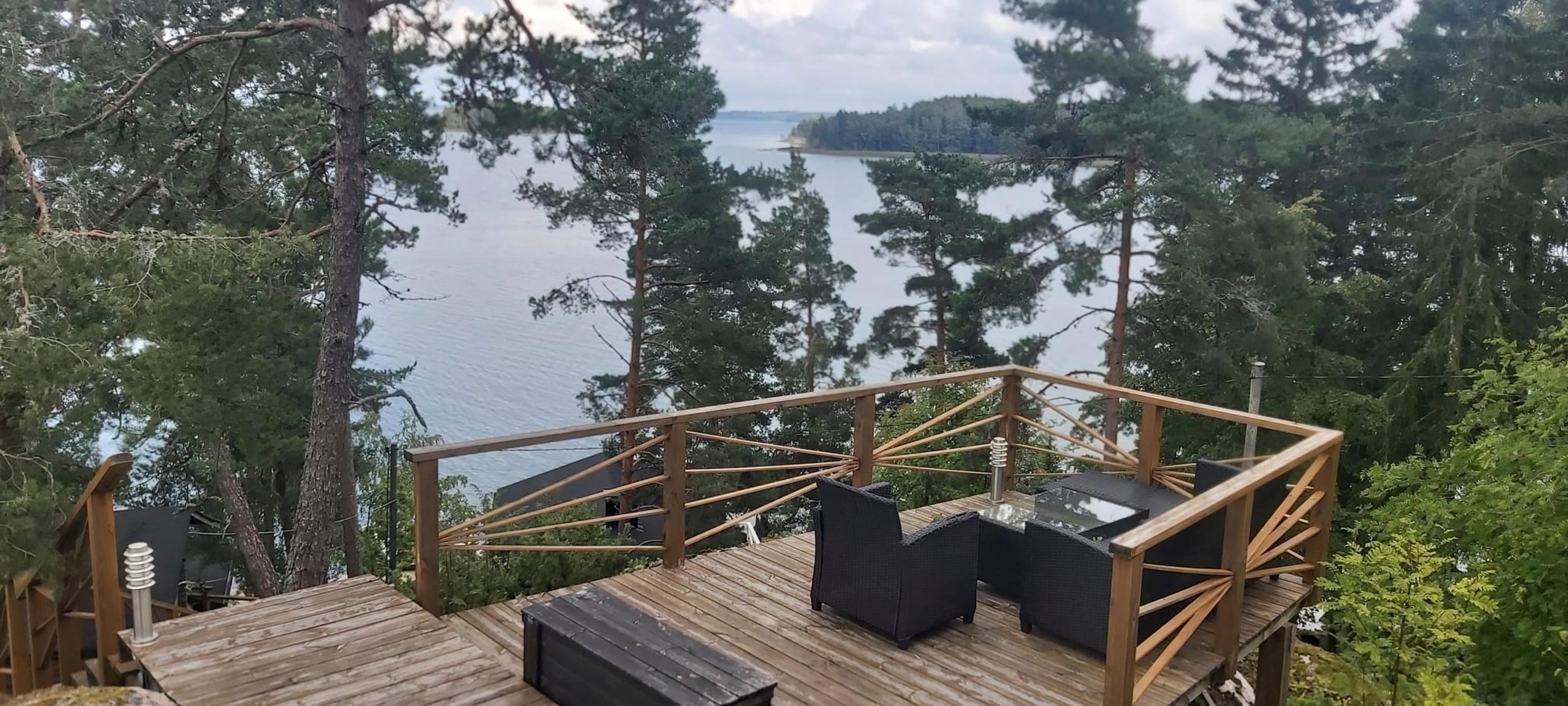 A patio set made of poly rattan on a terrace high on a hill, a wooden railing with a sea view, pine trees