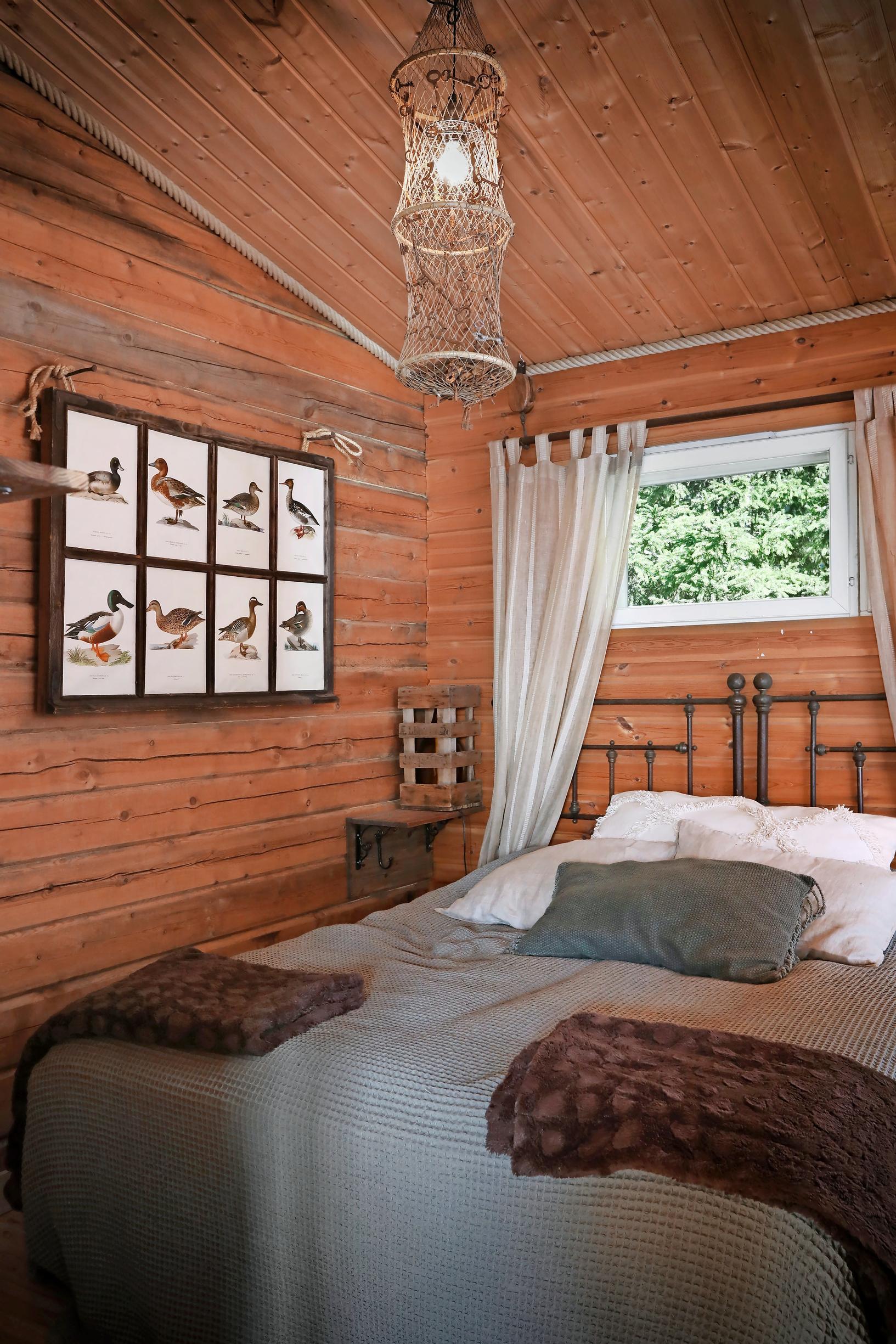A decorative piece made from an old window featuring bird pictures, a bed, light curtains on the window, and a log wall.