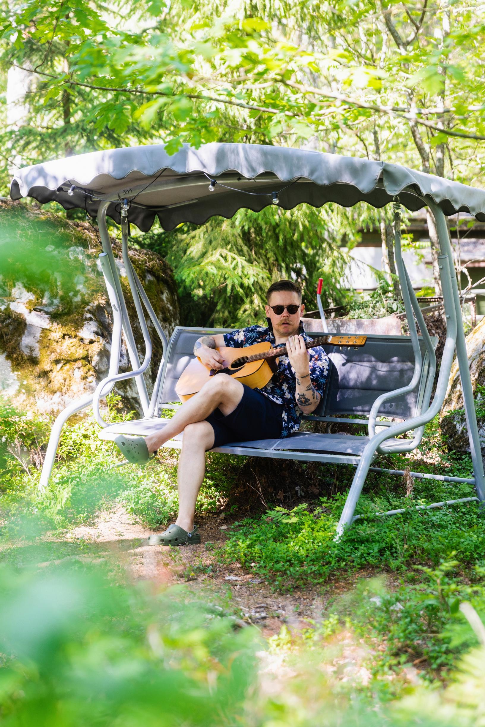 Pasi sitting in a garden swing playing guitar