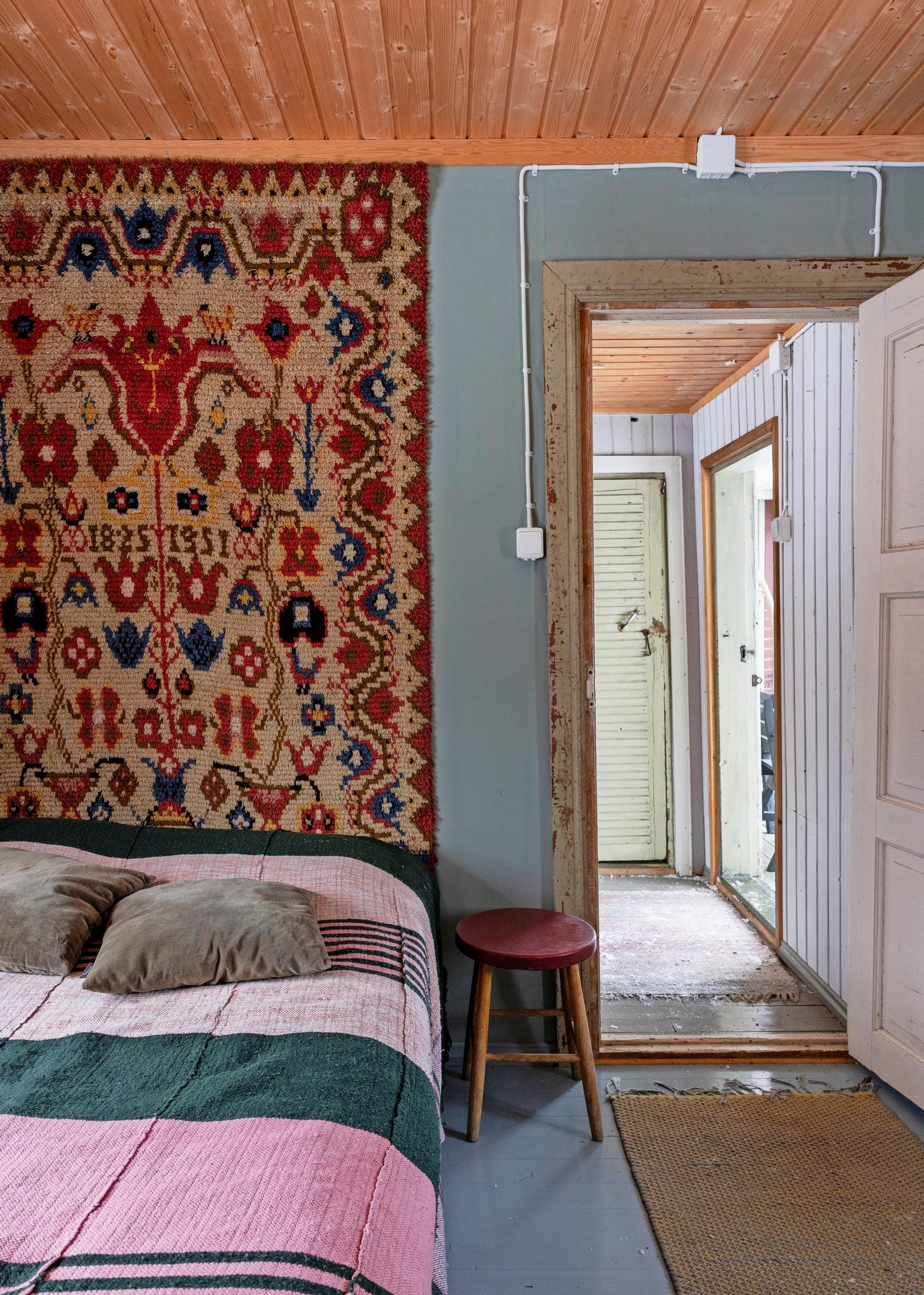 A large wall rug in the bedroom, colorful bedspread, and stool