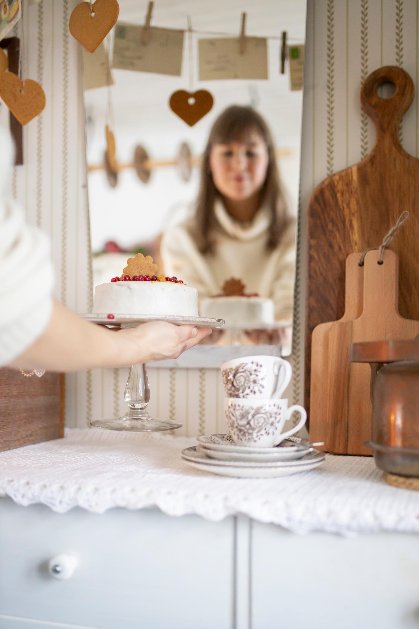A woman lifting a cake with coffee cups on a sideboard.