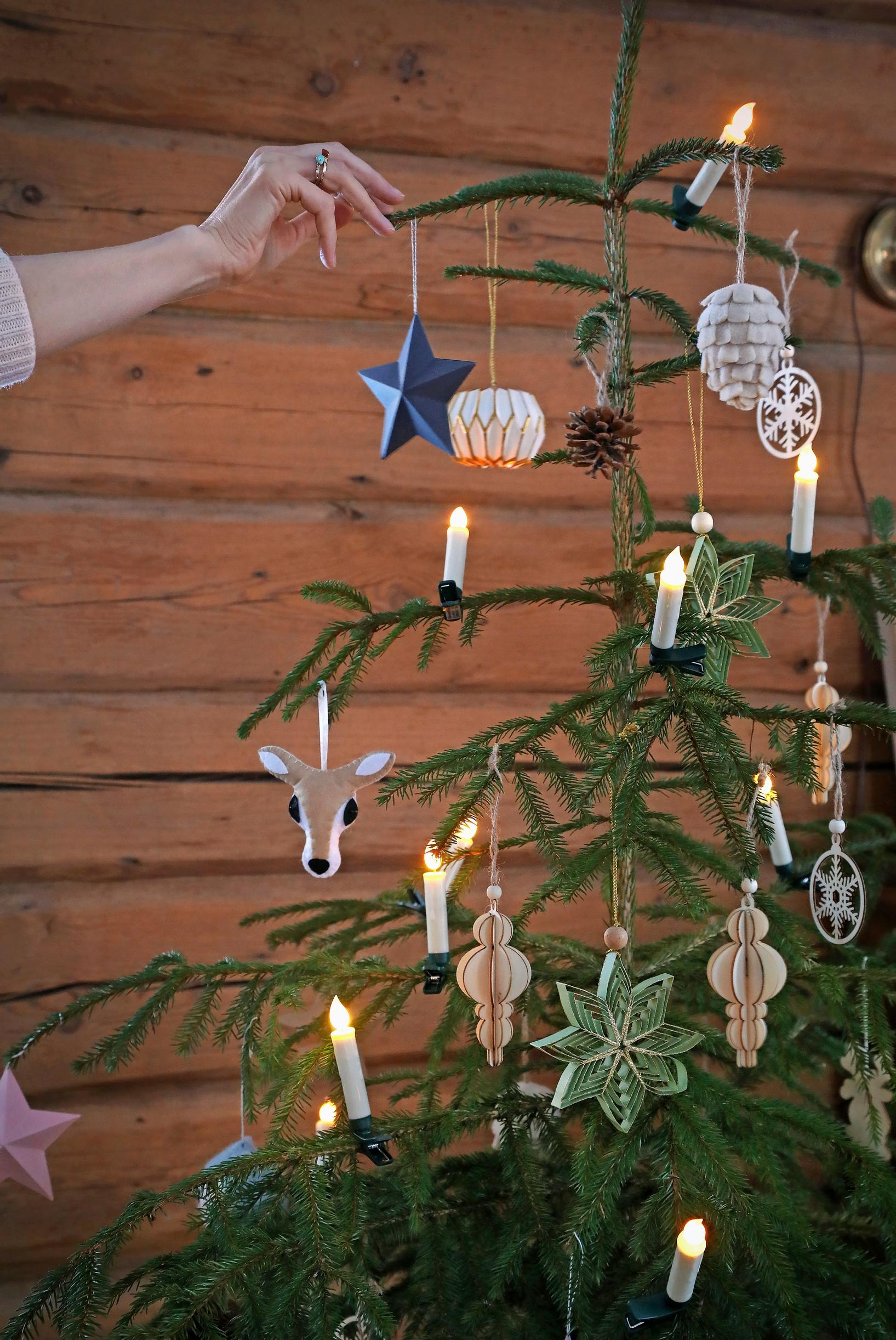 Ulla’s hand hanging an ornament on the Christmas tree, with a log wall in the background.