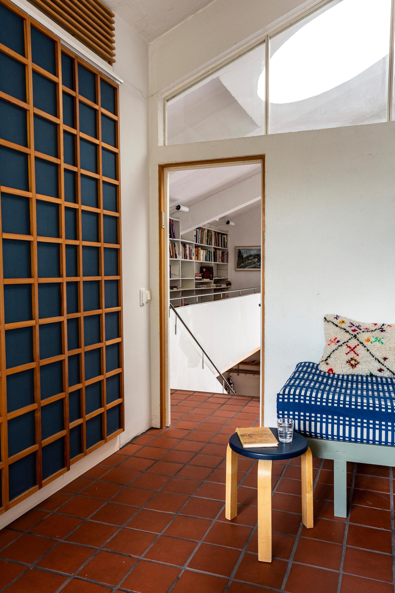 A grid-paneled cabinet door, terracotta-tiled floor, Artek stool, and part of a bed