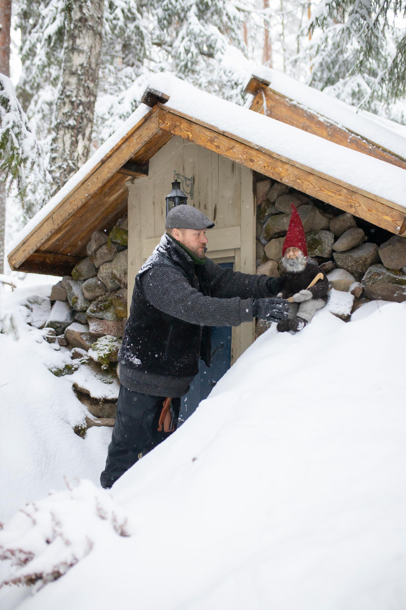 A man placing a gnome ornament in the snow by the root cellar.