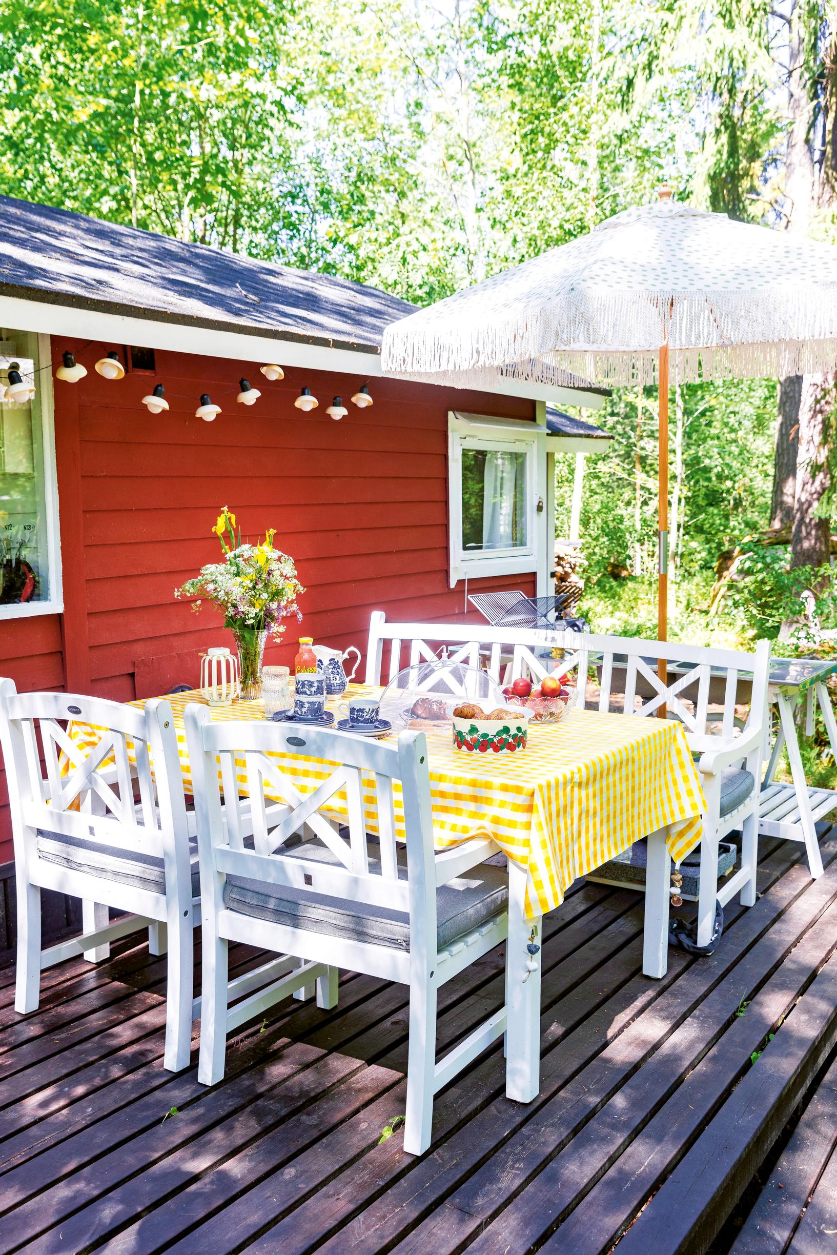 a white dining set on a terrace in front of a summer cabin