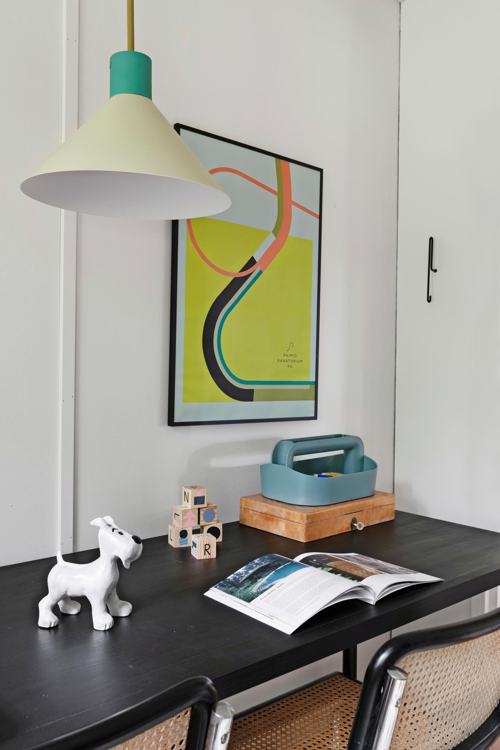 A black writing desk, two chairs, objects on the table, and a colorful painting.