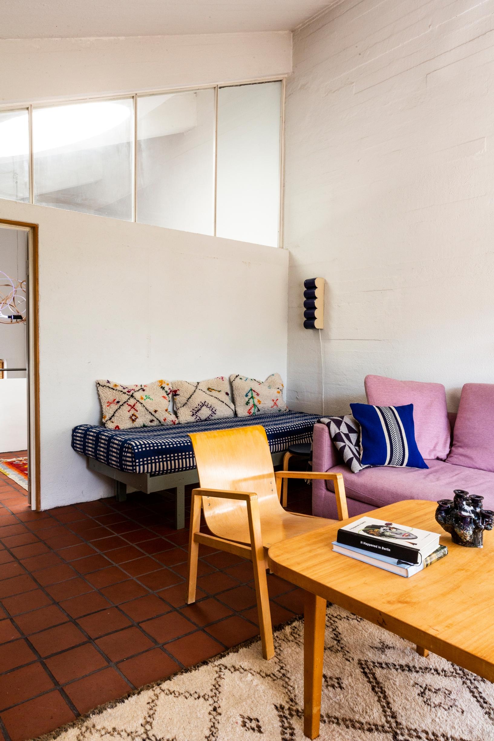 A wooden chair and table, pale lilac sofa, and a bed used as a couch