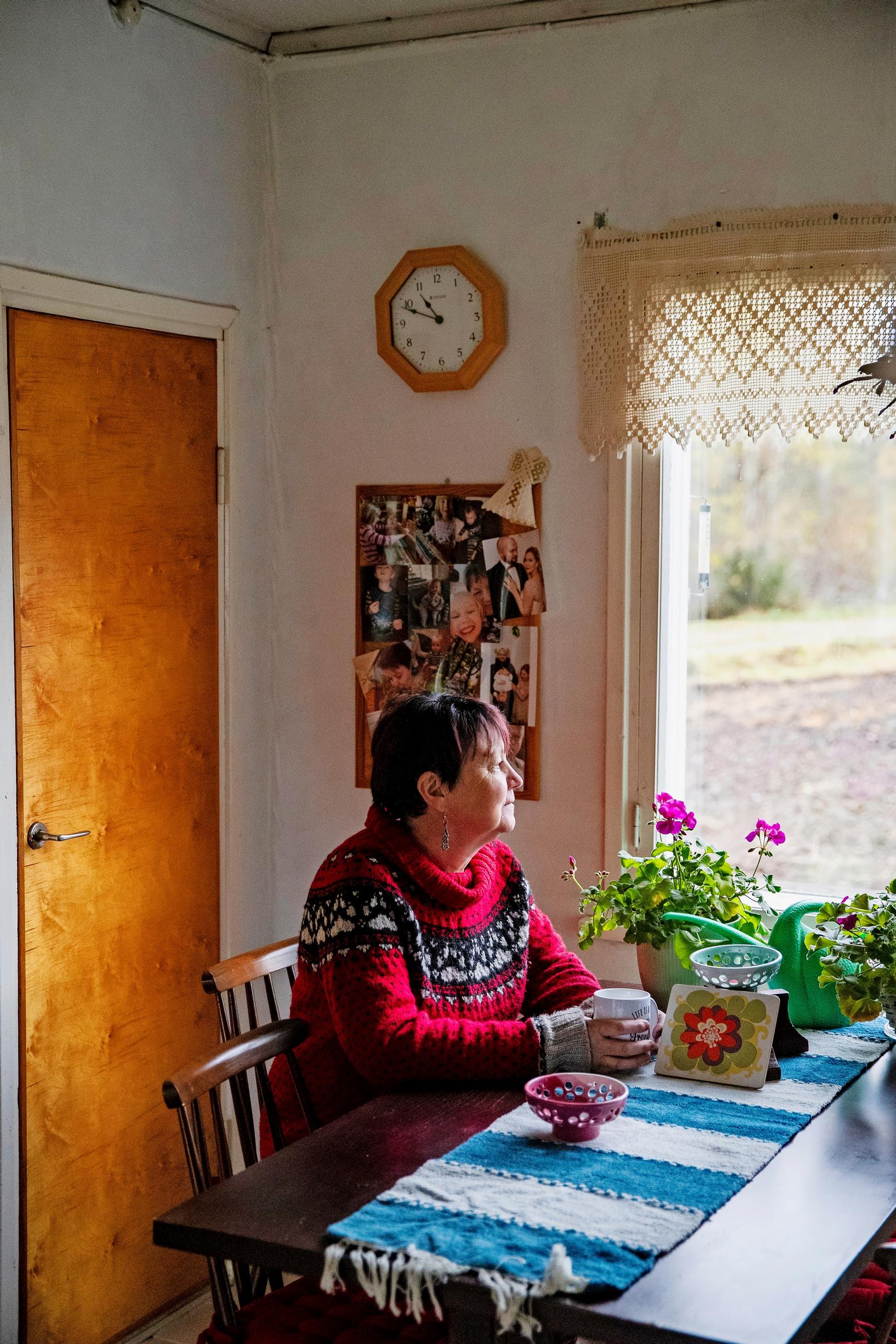 Päivi sits at the kitchen table and looks out the window.