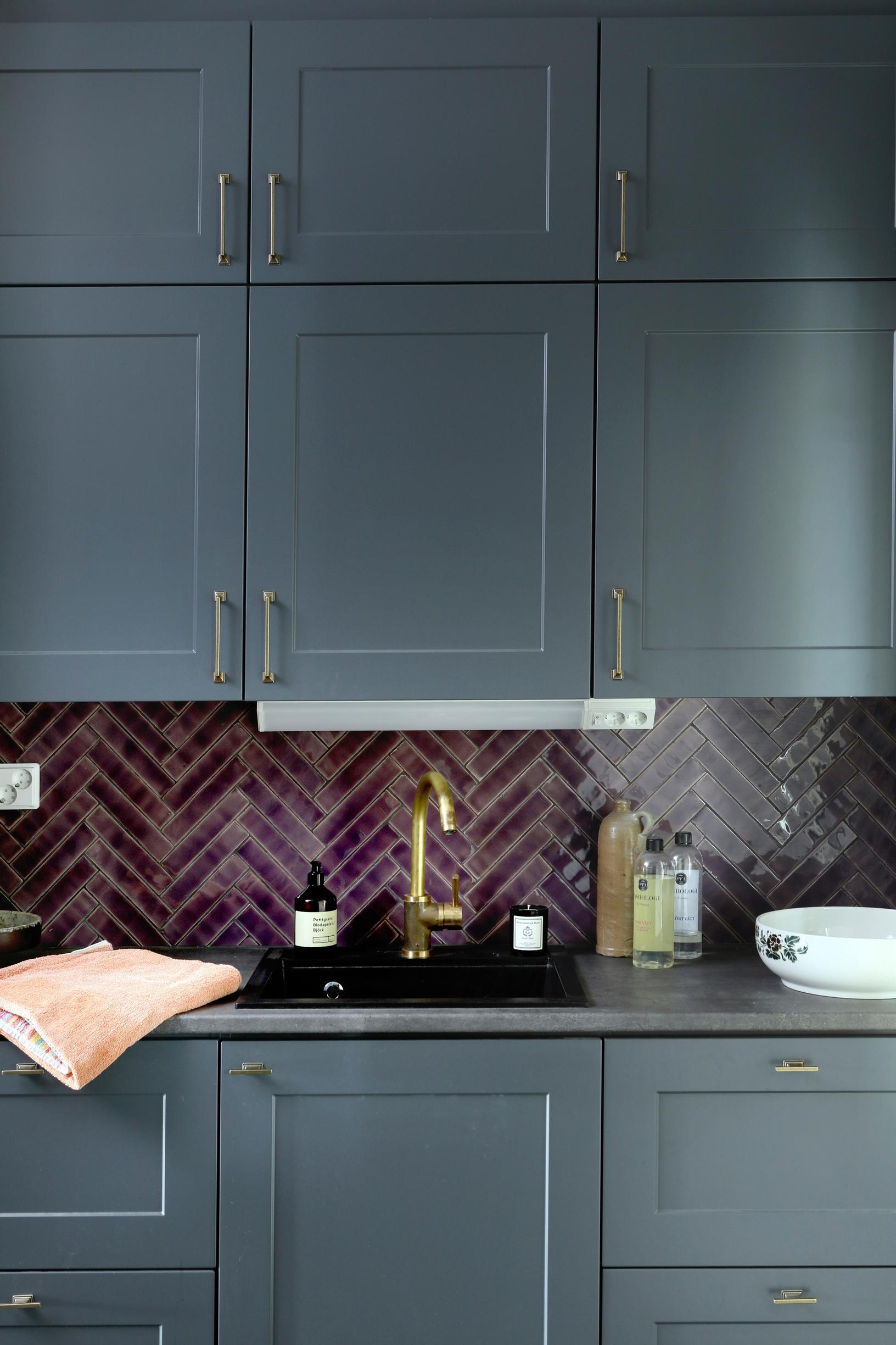 Kitchen with gray cabinets and burgundy backsplash tiles.