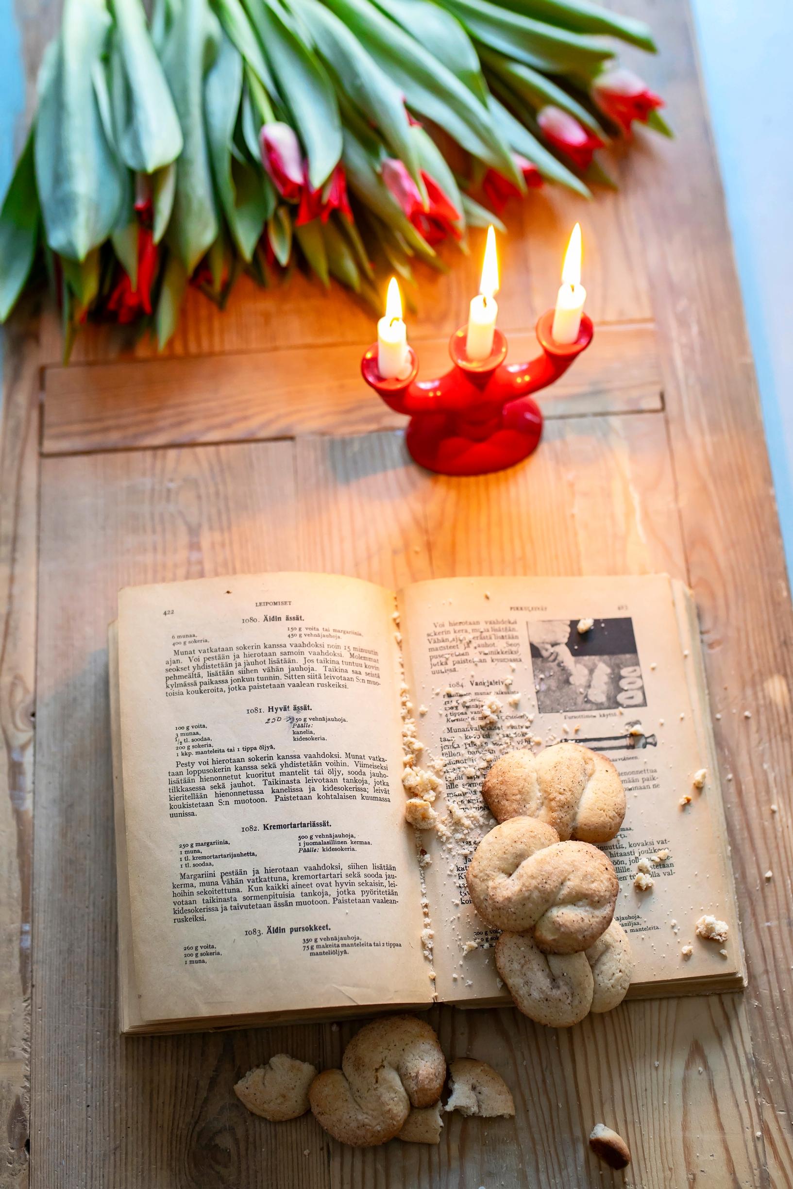 Tulips, a small candle holder, an old book, and cinnamon S-cookies on a table