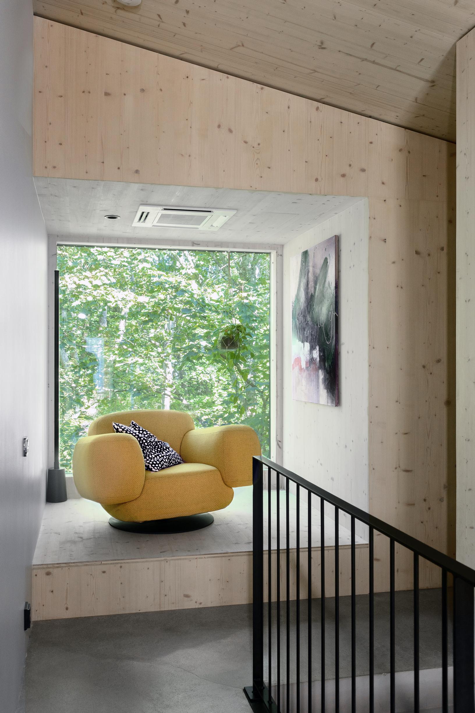 A yellow armchair stands in front of the large window in the CLT home.