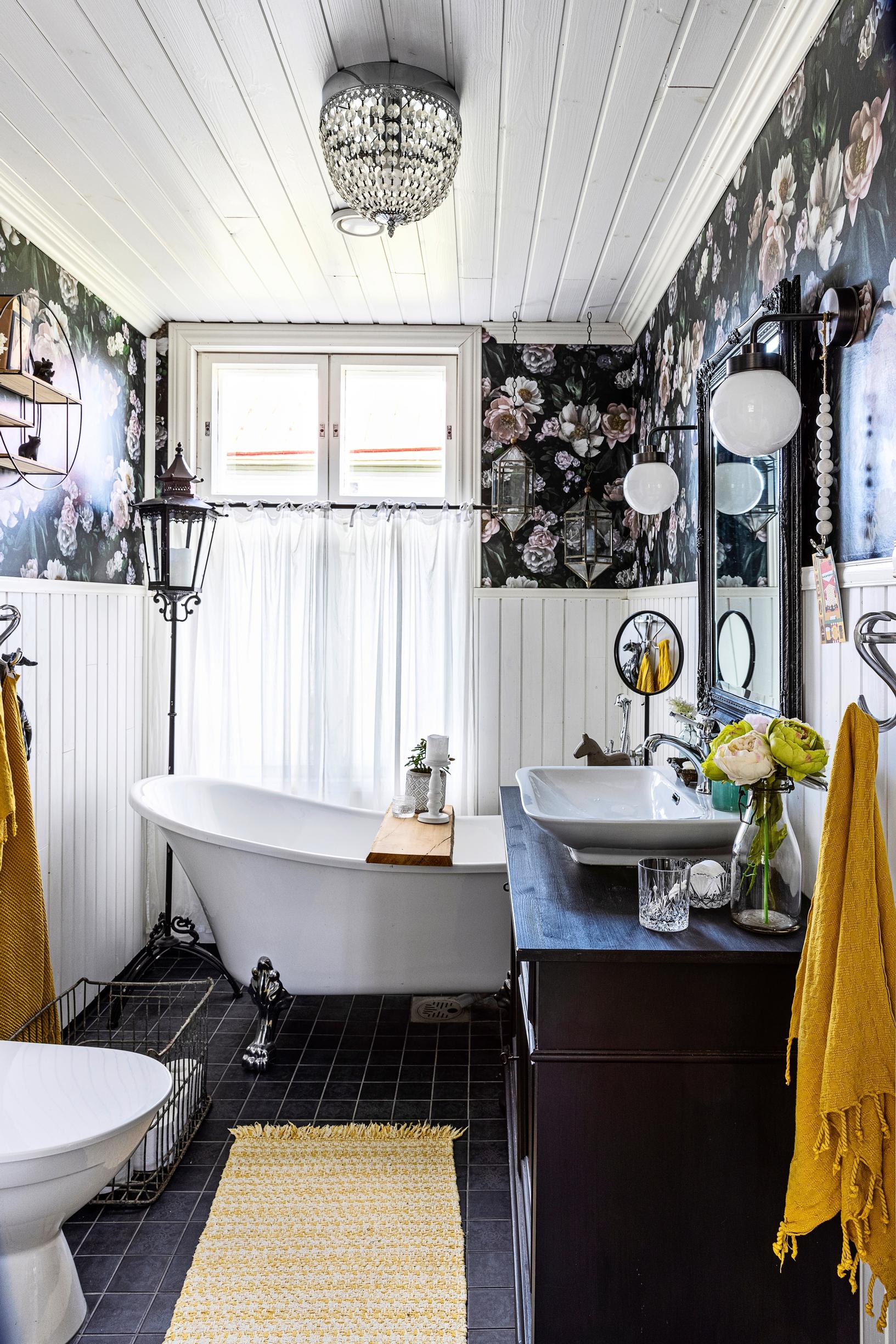 A bathroom in an old house with dark floral wallpaper and white half-paneling.