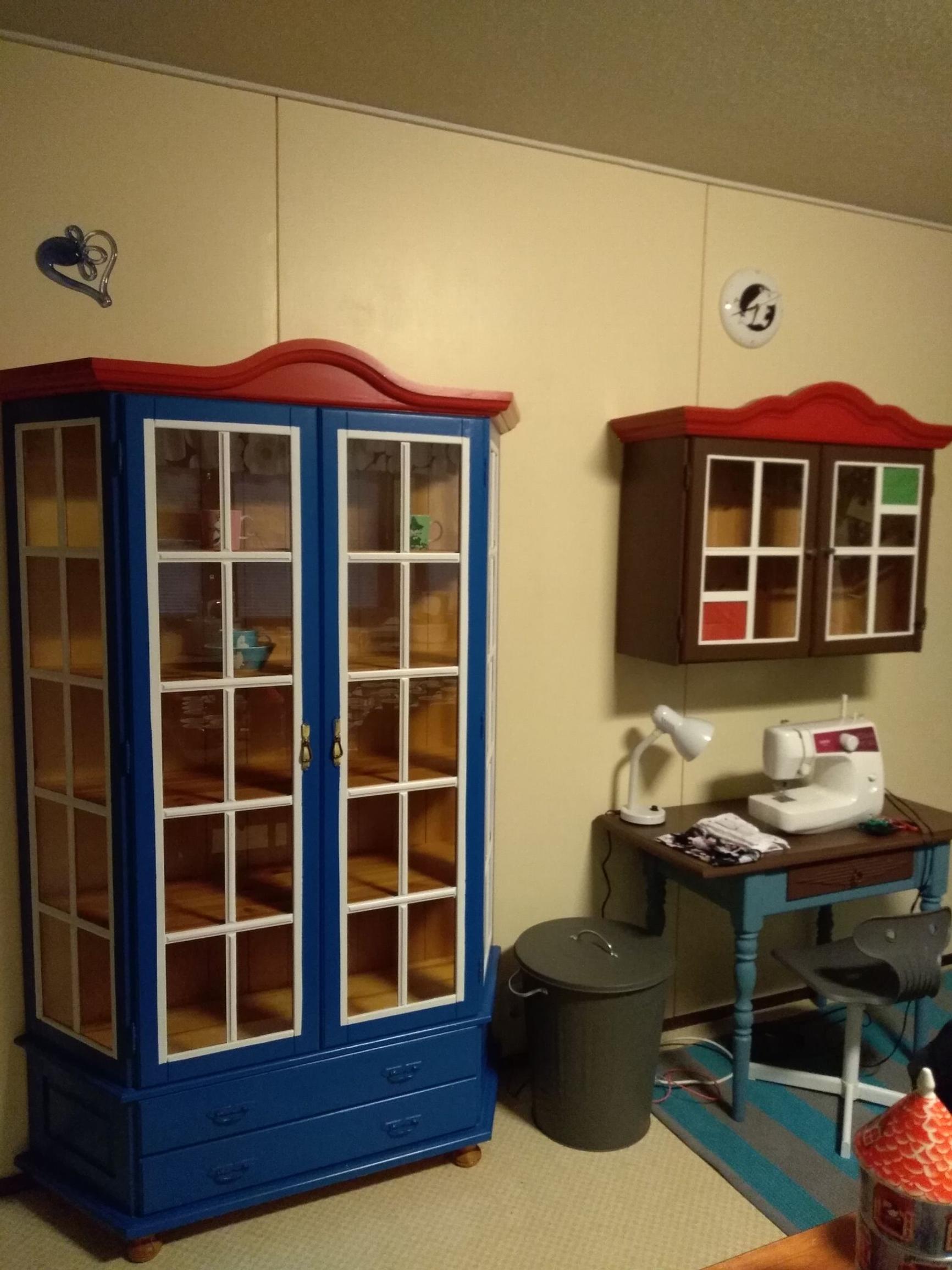 A blue display cabinet with a red roof and a wall cabinet, both Moomin-themed