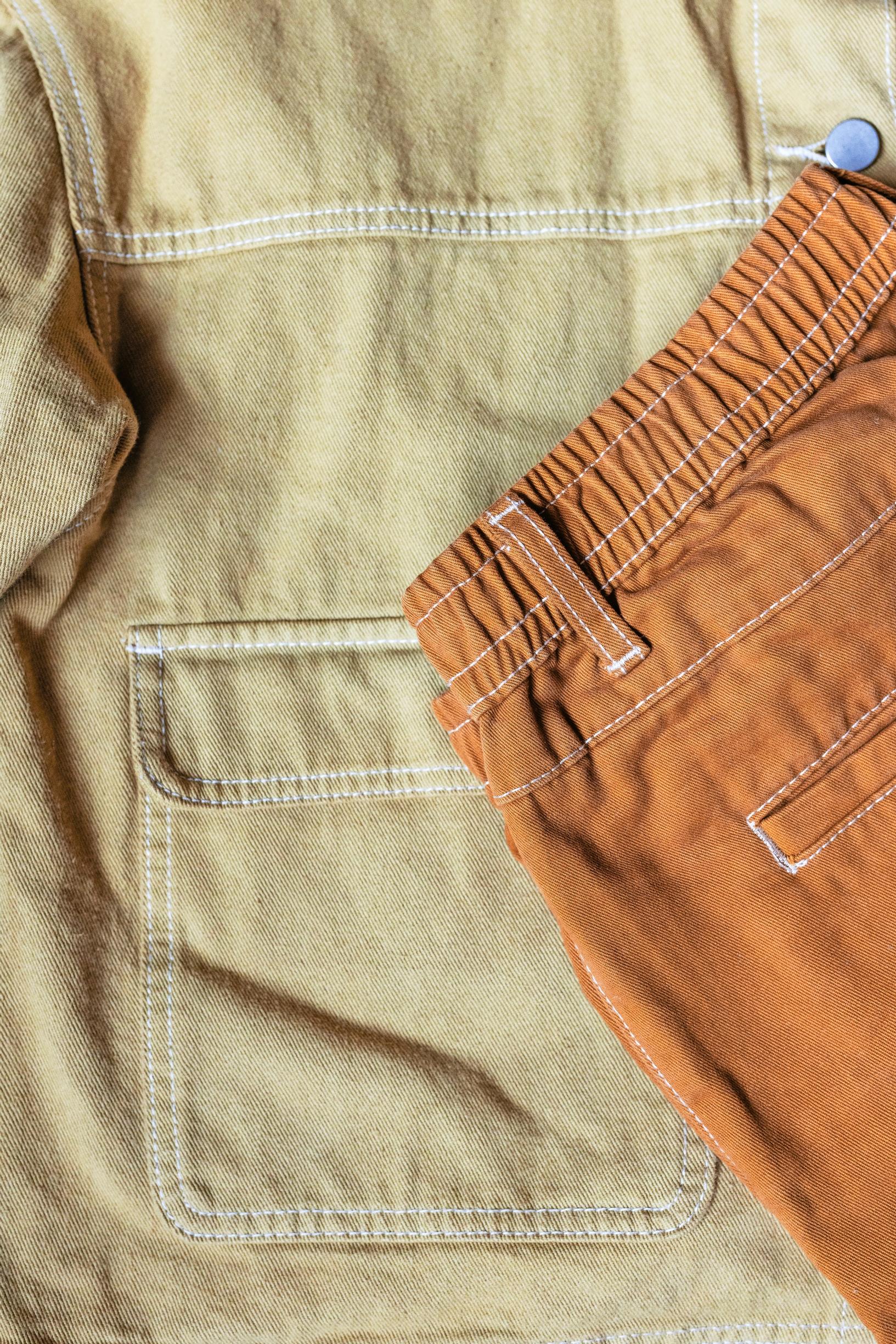 Two pairs of pants dyed in yellowish hues, with white seam threads.
