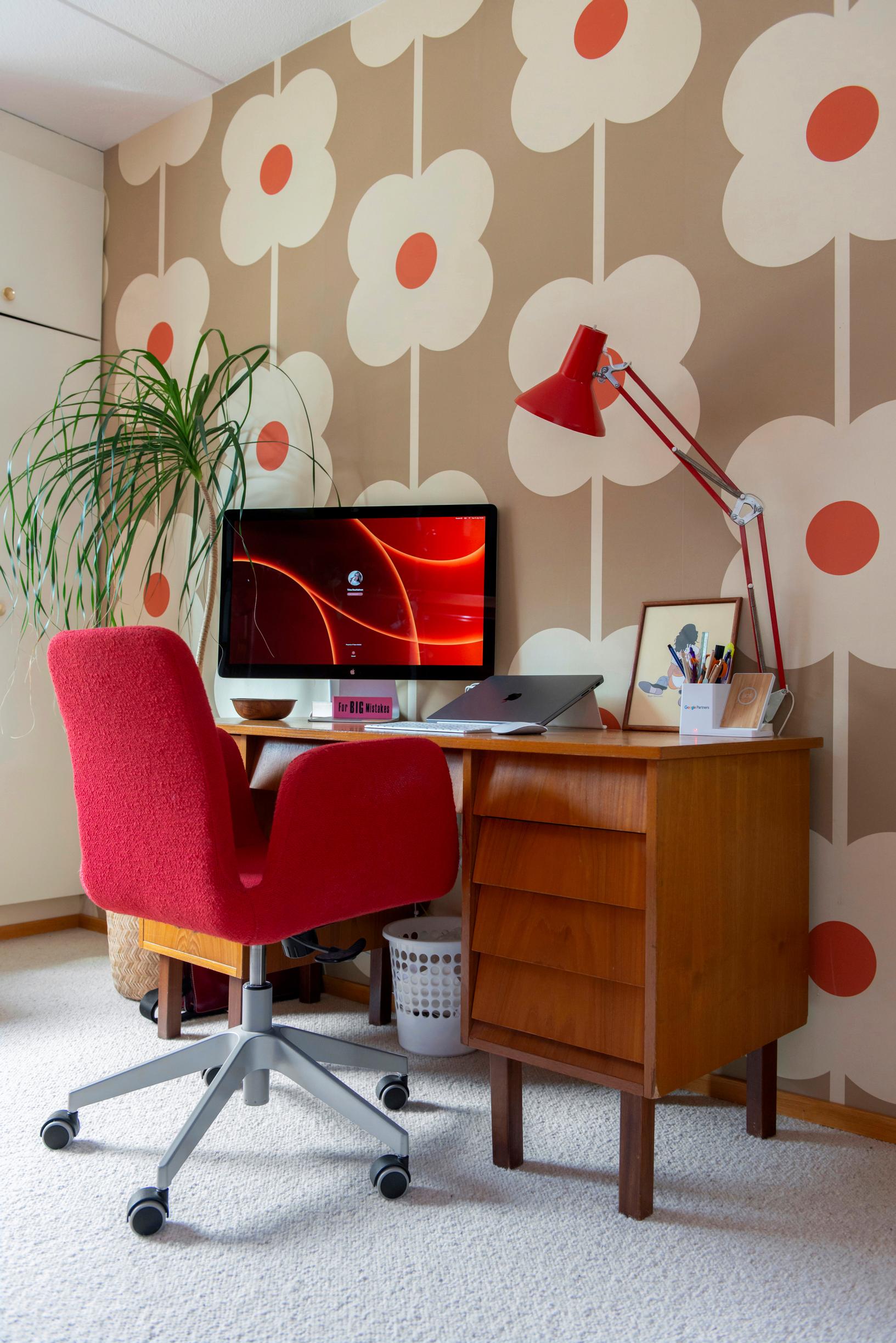 The wallpaper with a beige background features large white flowers with orange-red centers. Against the wall is a desk with chairs.