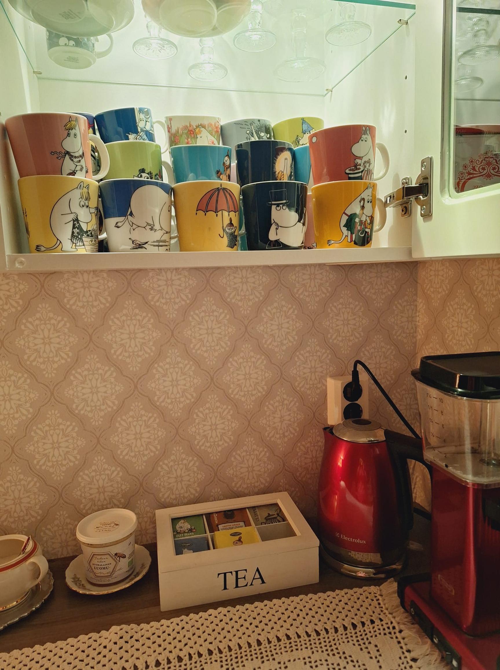 In the kitchen: a tea box and kettle, with Moomin mugs on the shelf above