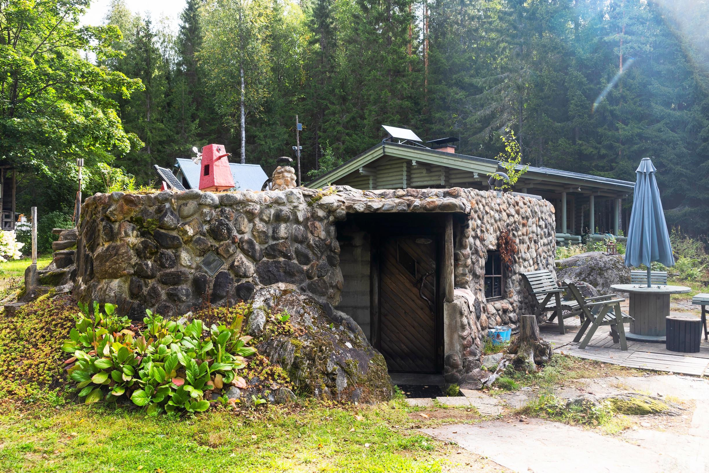A sauna built from natural stones, with bergenia, a sauna cottage in the background, and a garden set beside it