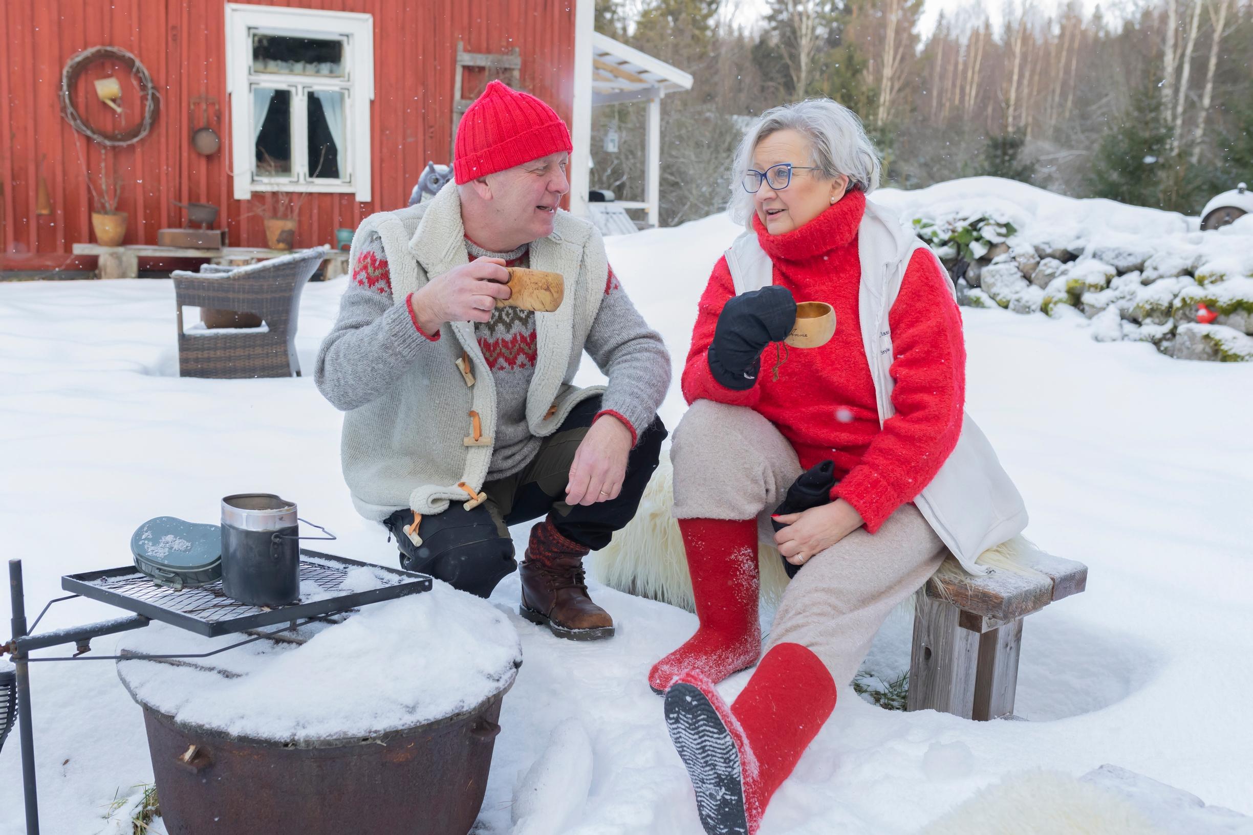 a man and a woman sit by a snowy grill spot with wooden cups in hand