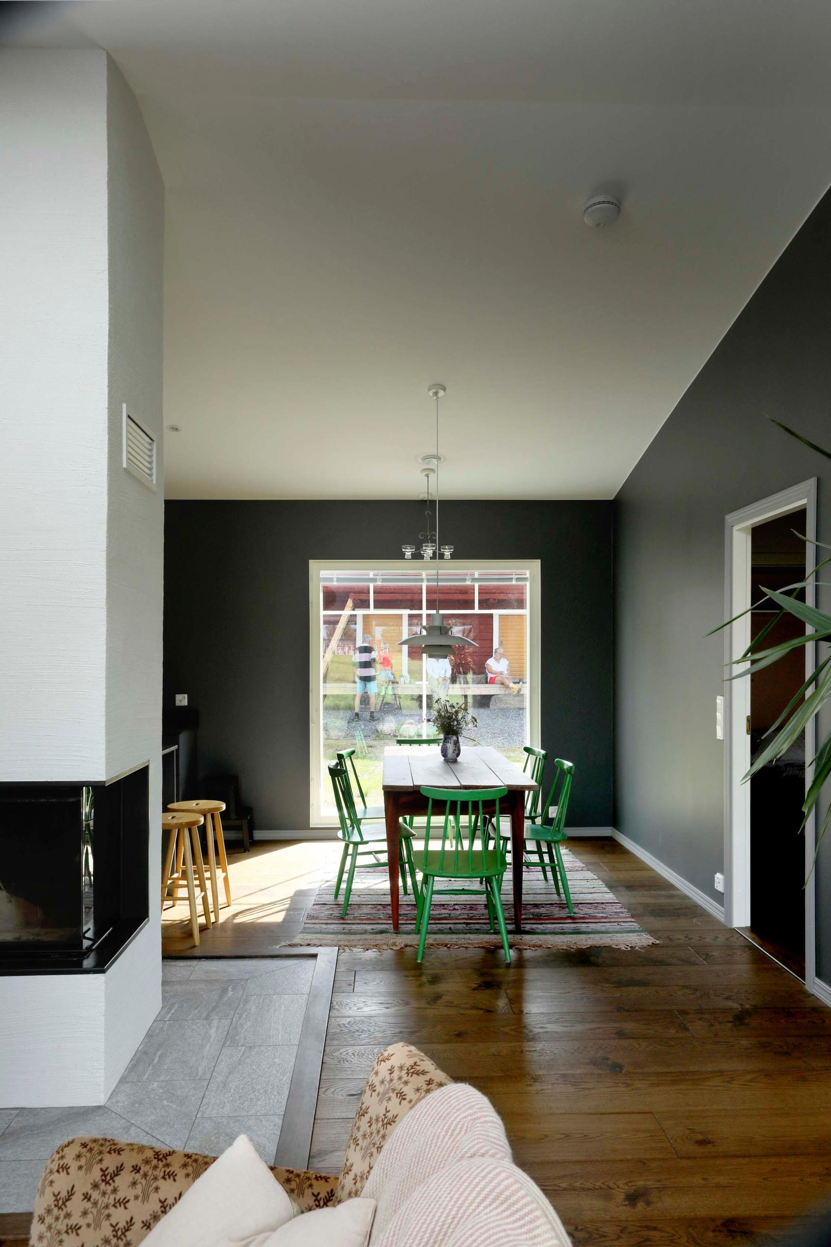 A white fireplace, dining area with dining set, and an outbuilding visible through the window.