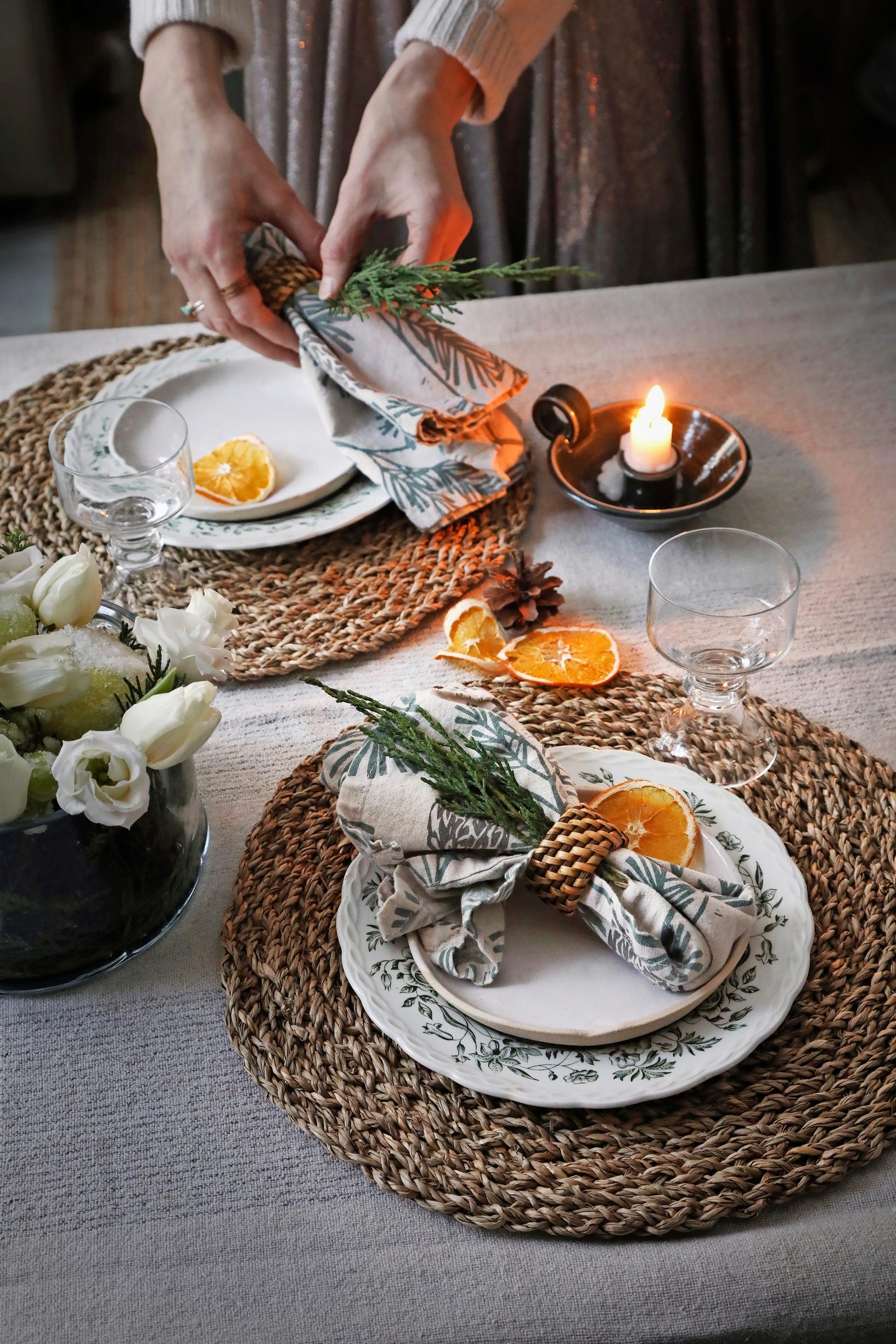 a festive table setting with plates and glasses on round placemats, decorated with cloth napkins and dried orange slices