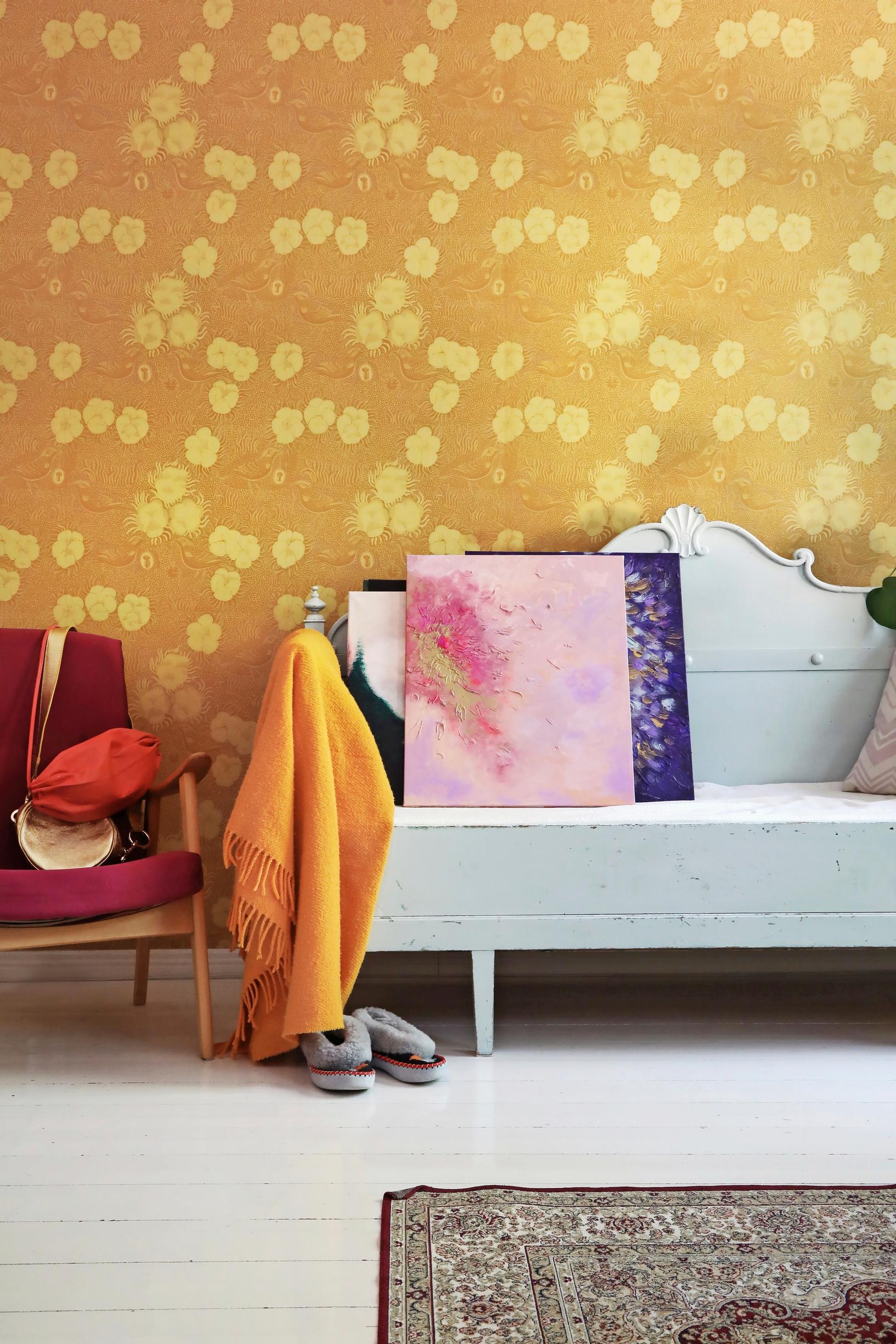 A photo of an old wooden sofa in a room with yellow Birger Kaipiainen “Kiurujen yö” wallpaper on the wall.