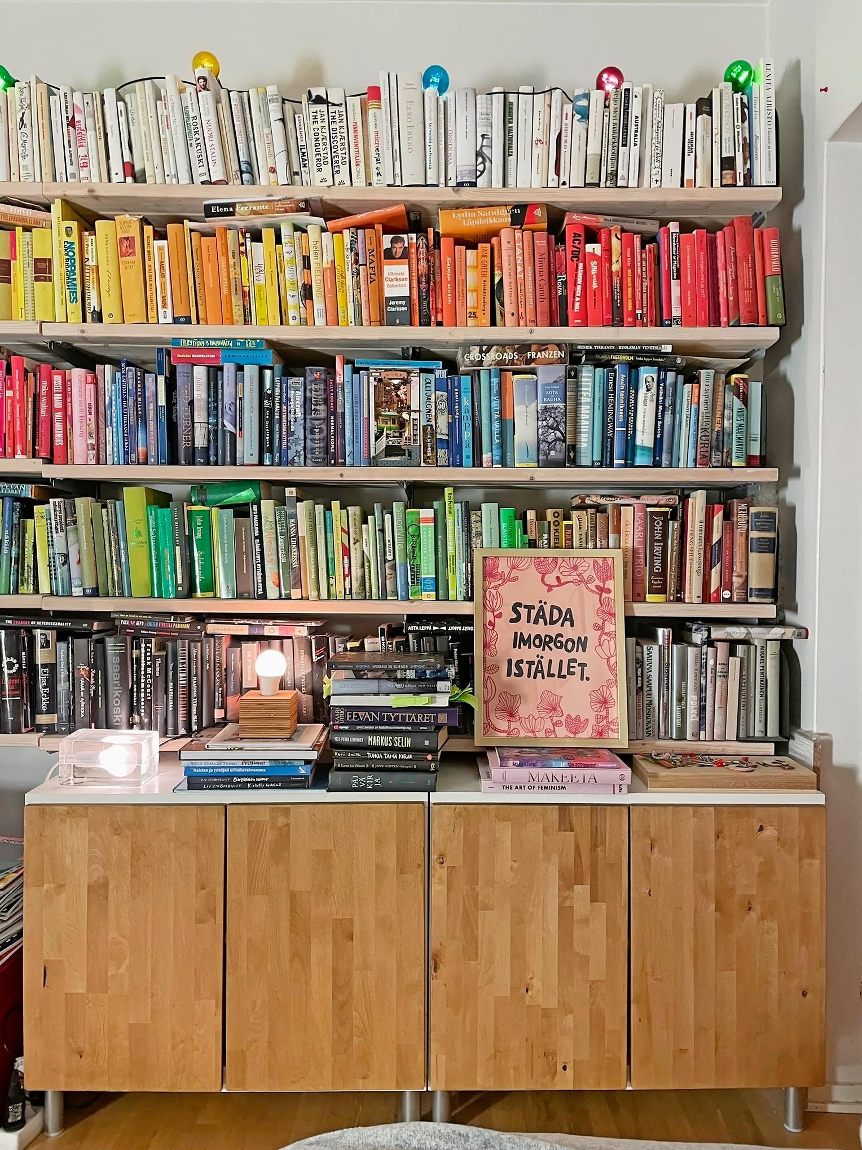 A bookshelf with color-organized books and wooden lower cabinets
