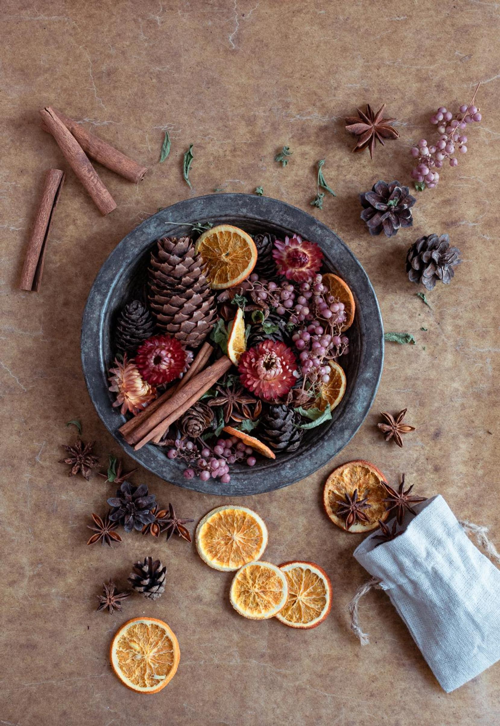 A potpourri of cones, cinnamon sticks, star anise, pink peppercorns, and dried orange slices.