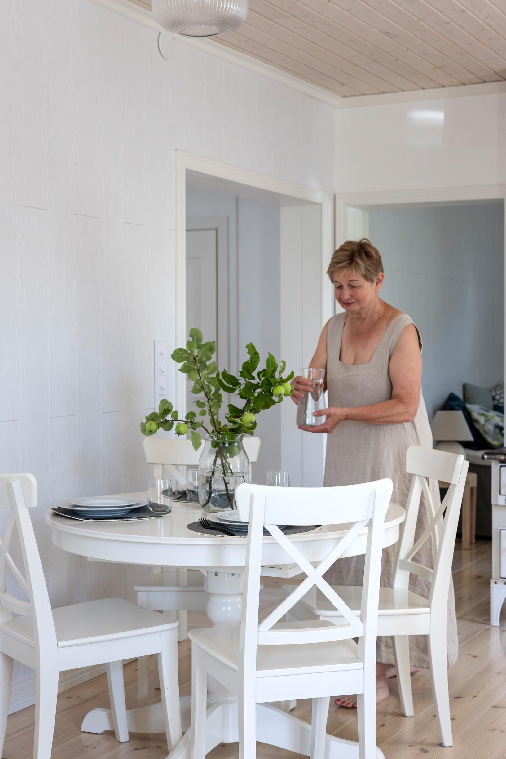 The interviewee stands behind the white dining table.