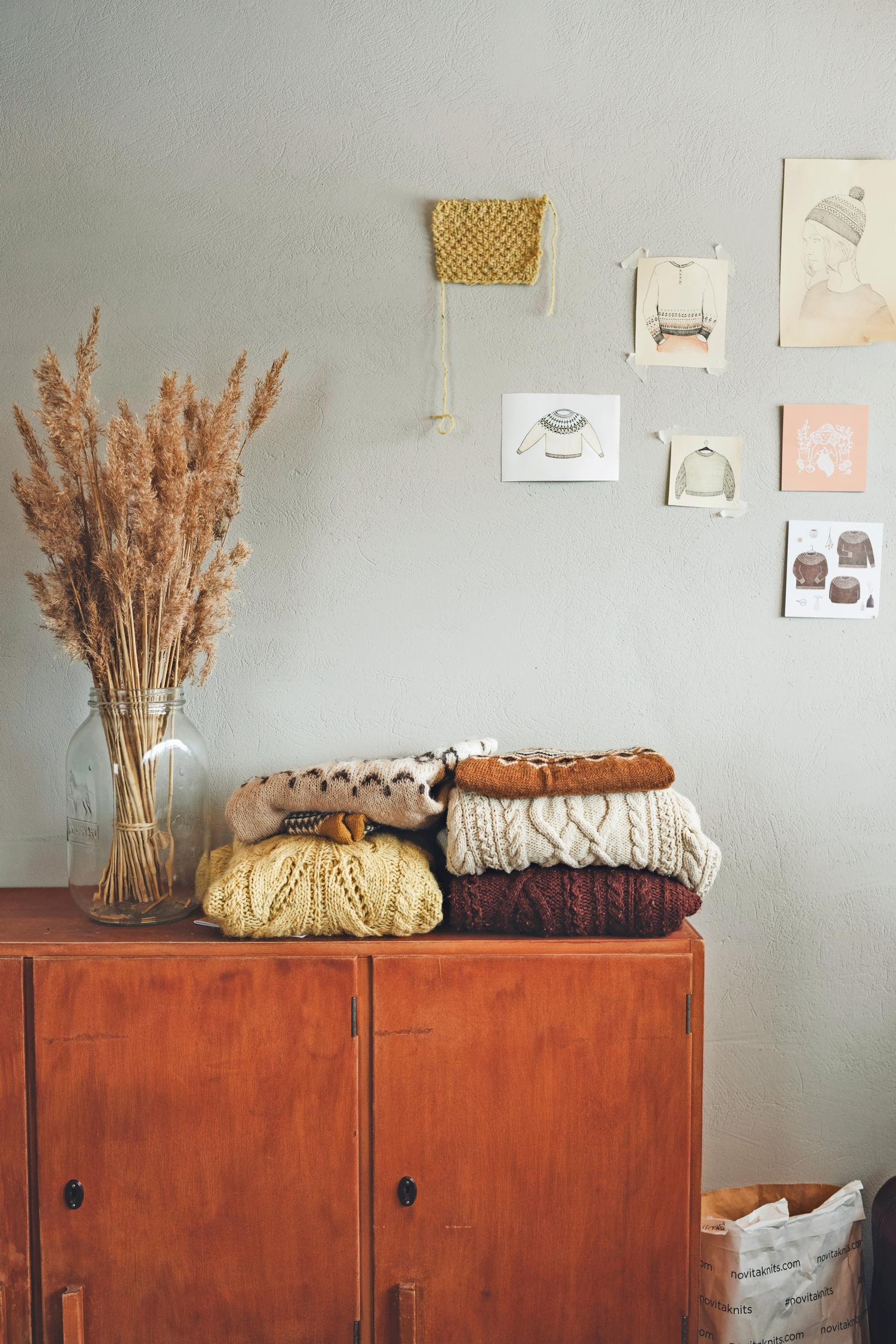 A peek into the workspace: knits on an old dresser, plus notes and sketches of knitting projects on a gray wall.