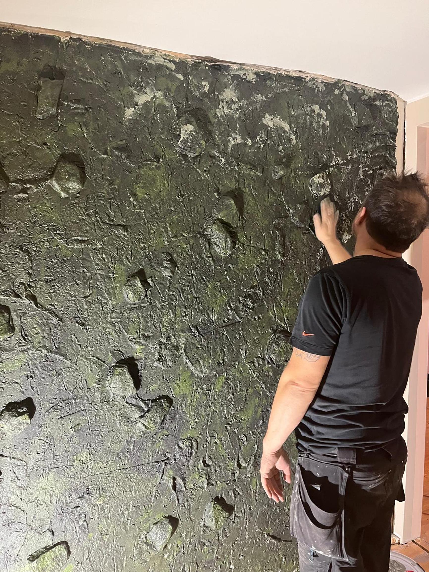 Kimmo smooths the green wall, which has an uneven surface.