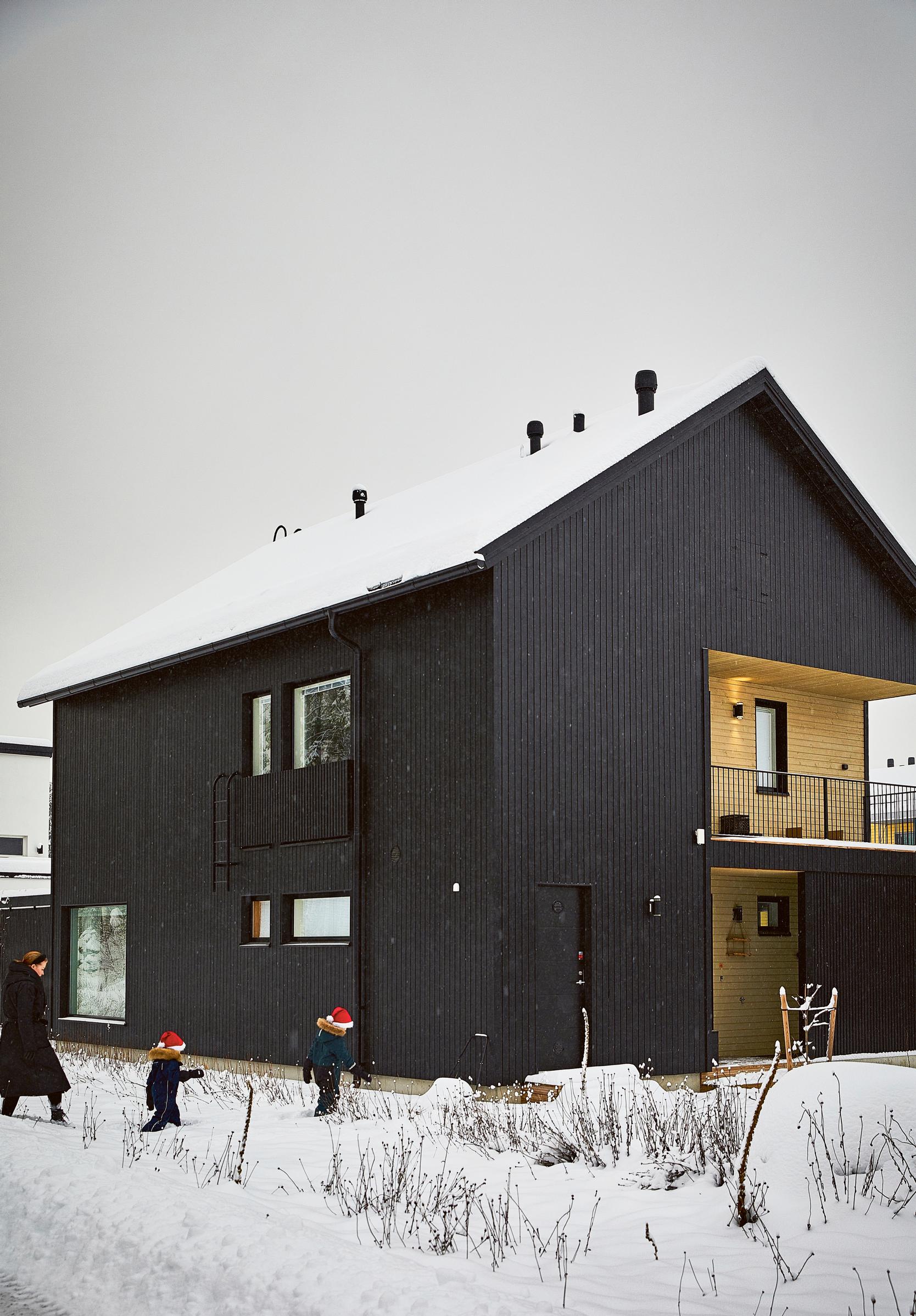 black single-family house, snow, a mother, and children wearing elf hats outside