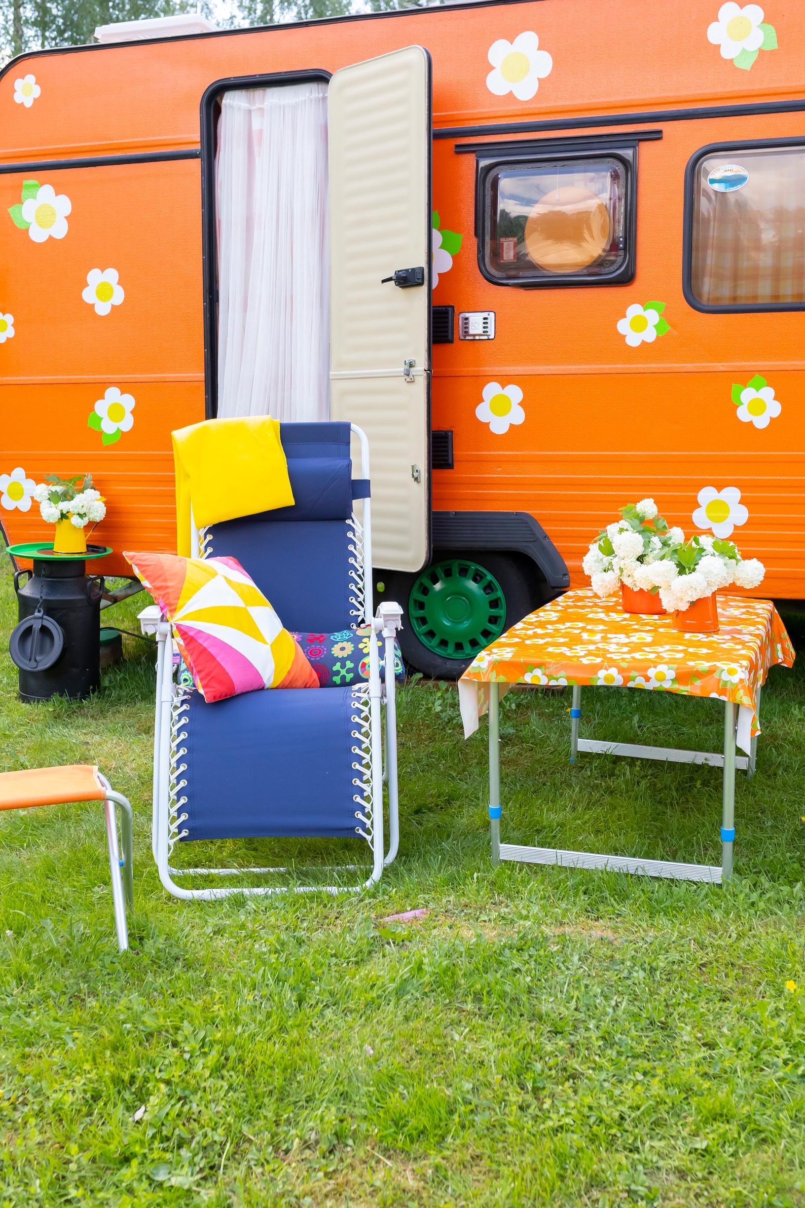an orange travel trailer, a blue patio chair, and a floral tablecloth on a garden table