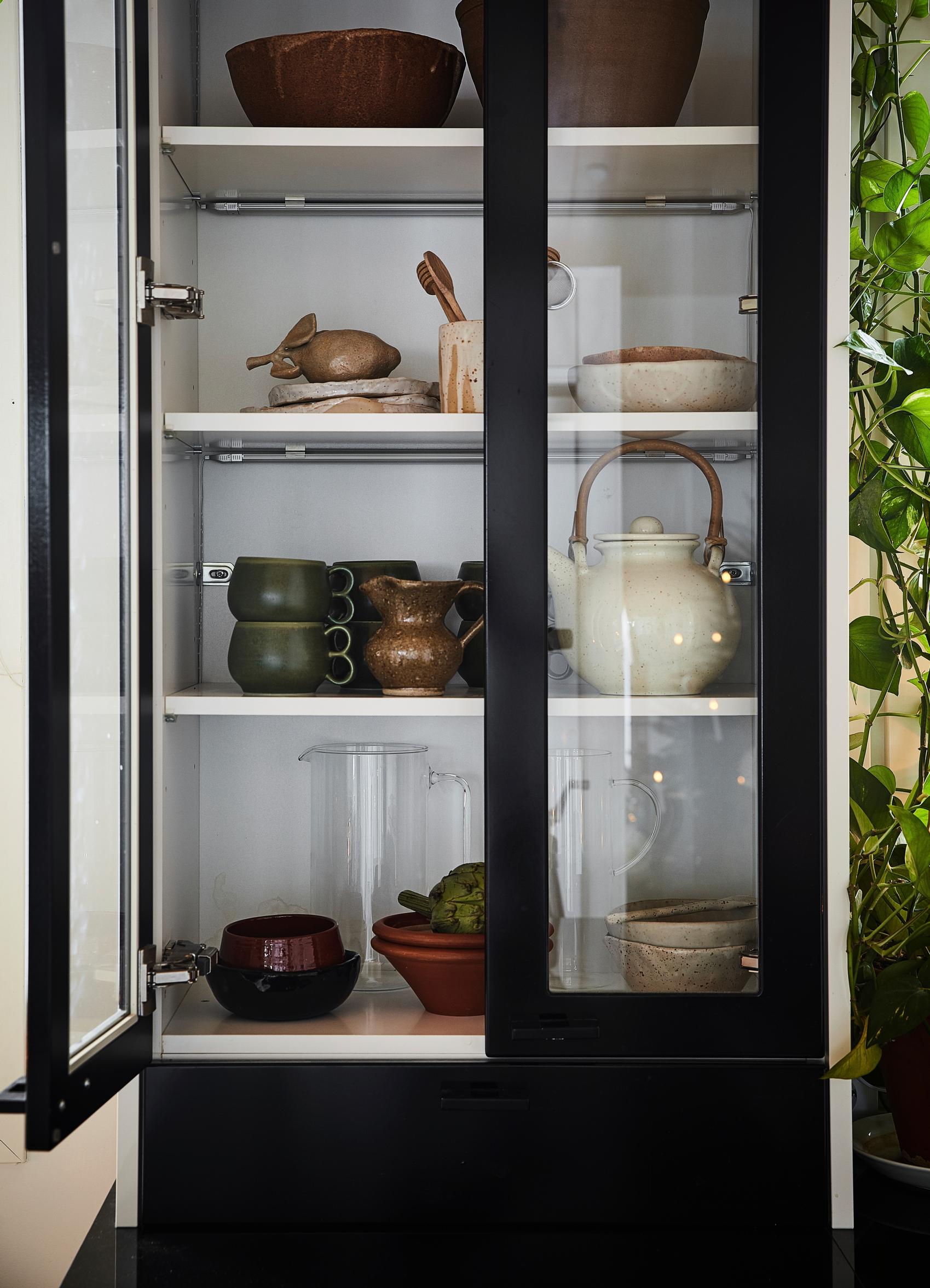 Ceramic dishes and glass jugs in a black china cabinet with glass doors