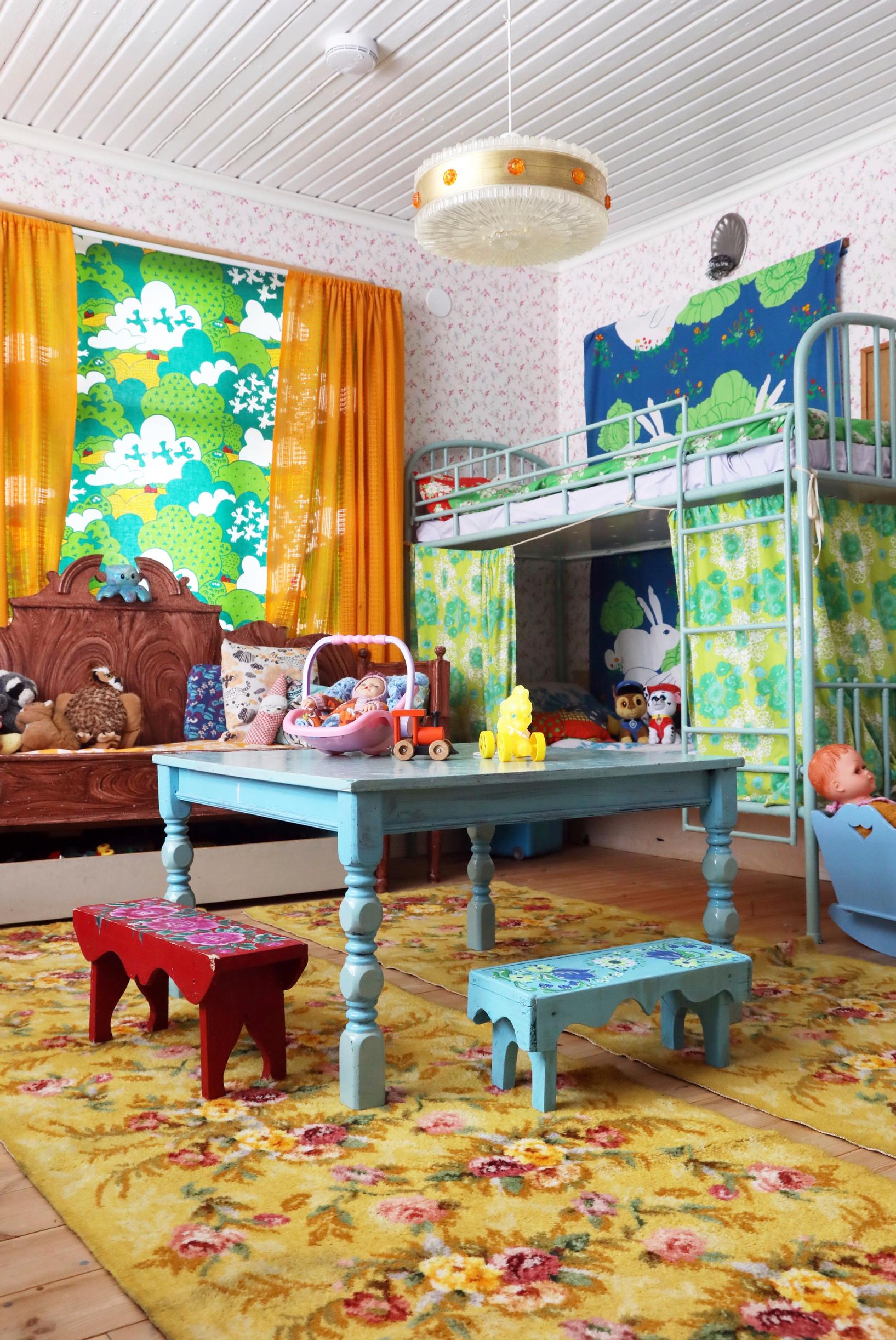 A colorful children’s room with a floral rug and painted wooden furniture.