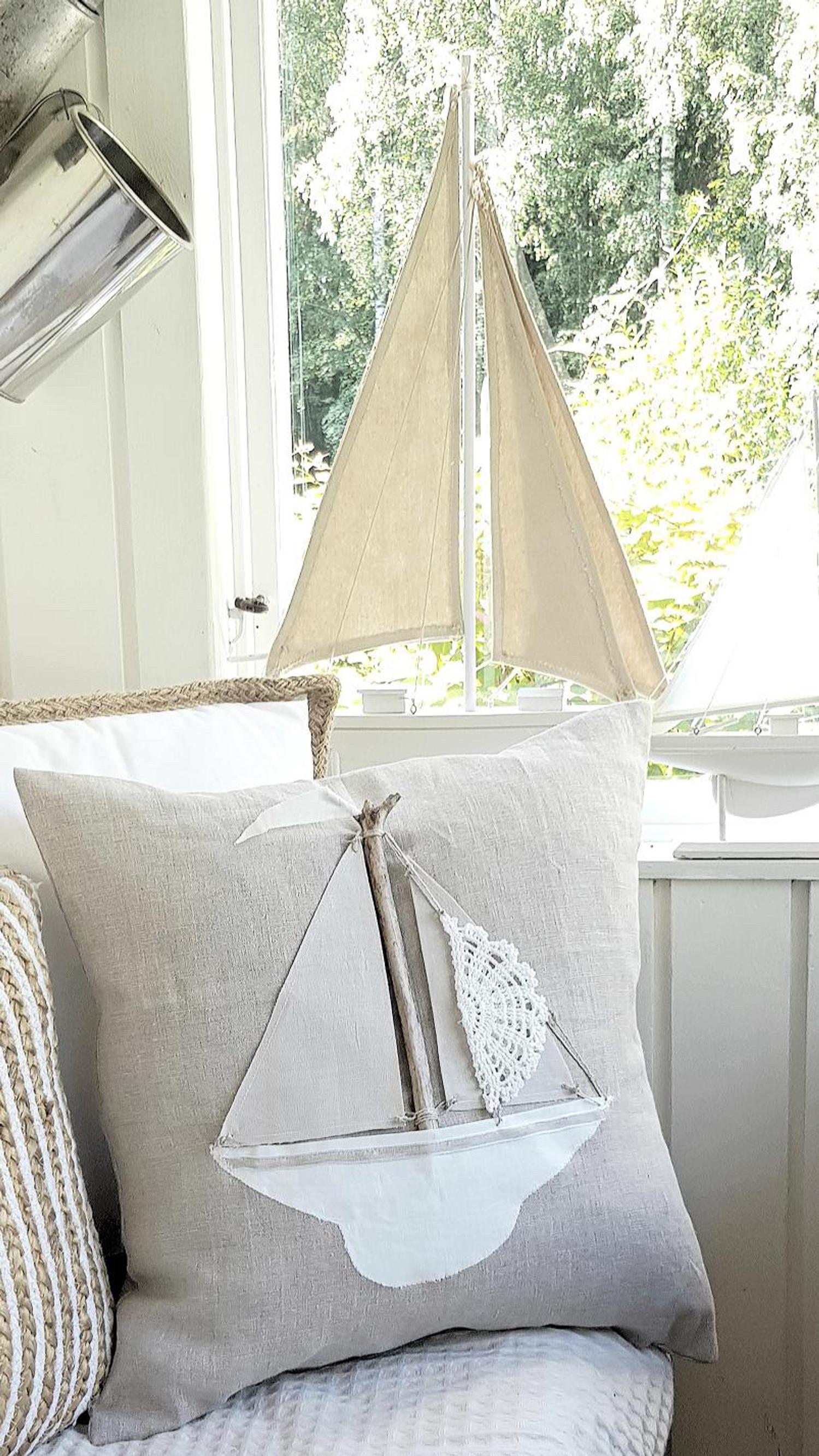 The throw pillow features a sailboat pattern. The sail is made of a lace doily.