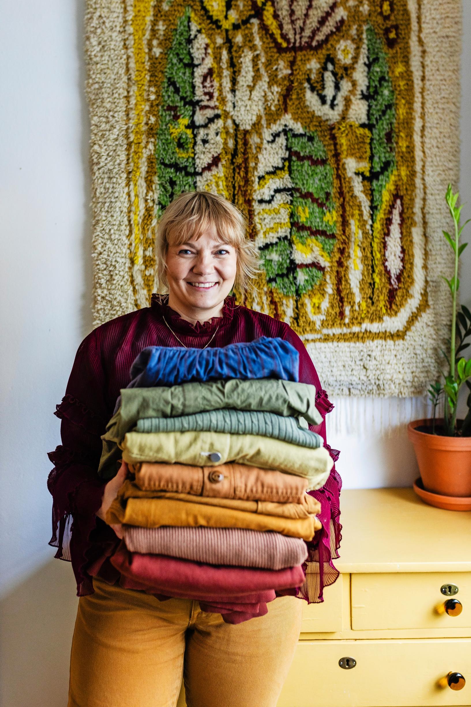 Suvi holding a stack of clothes in various colors.