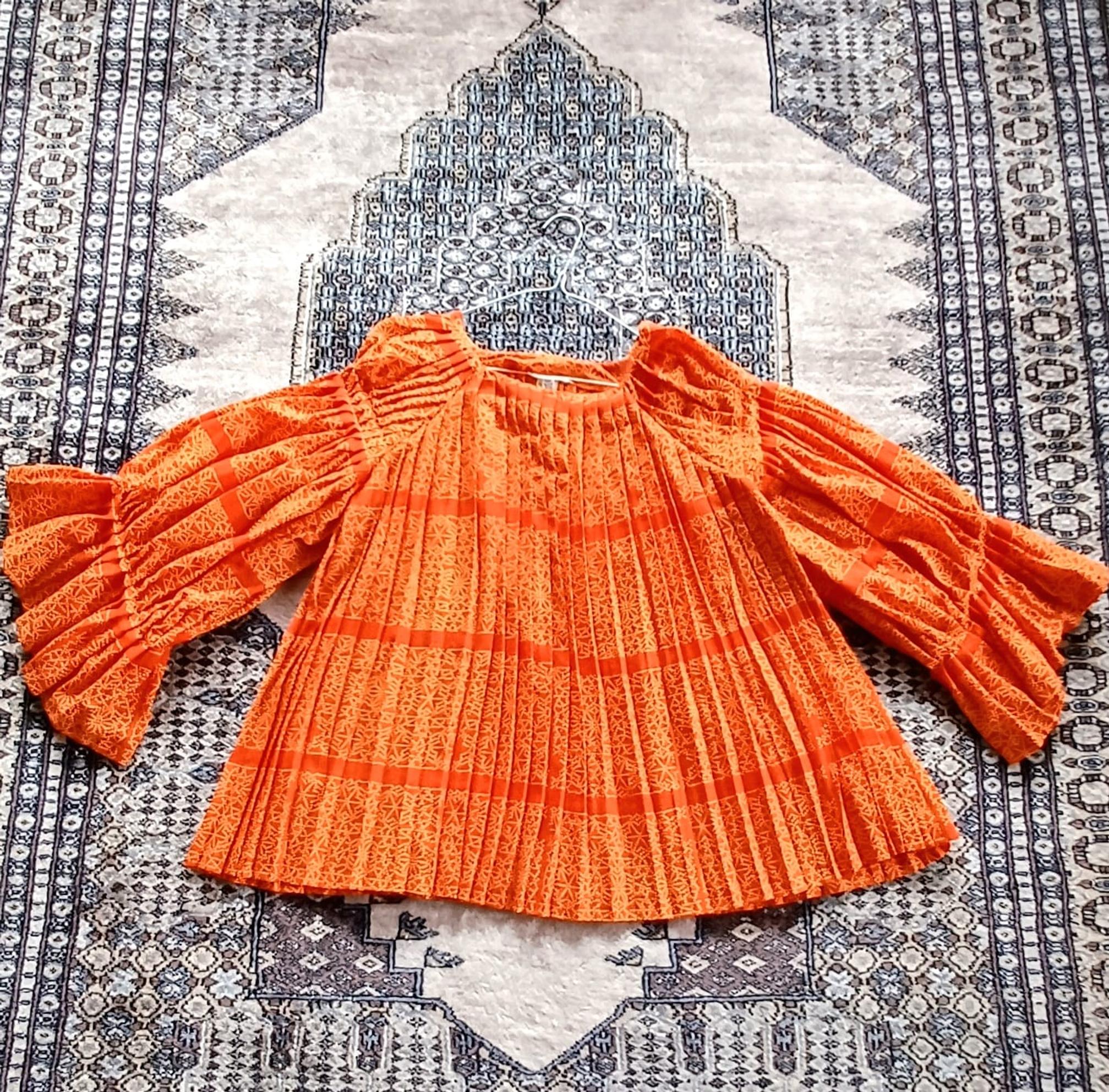 An orange pleated tunic spread out on a rug