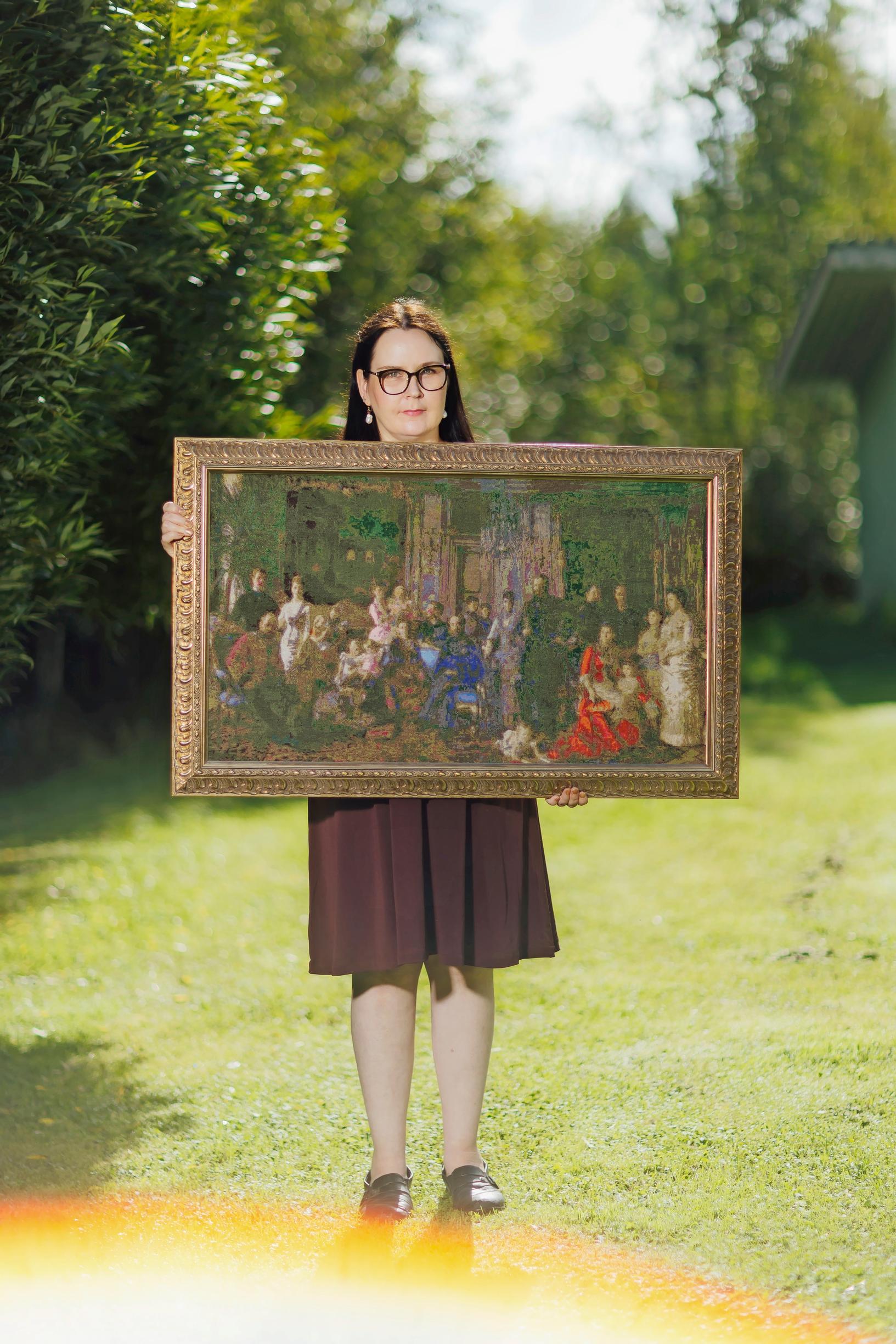 Tanja standing and holding her large cross-stitch piece.