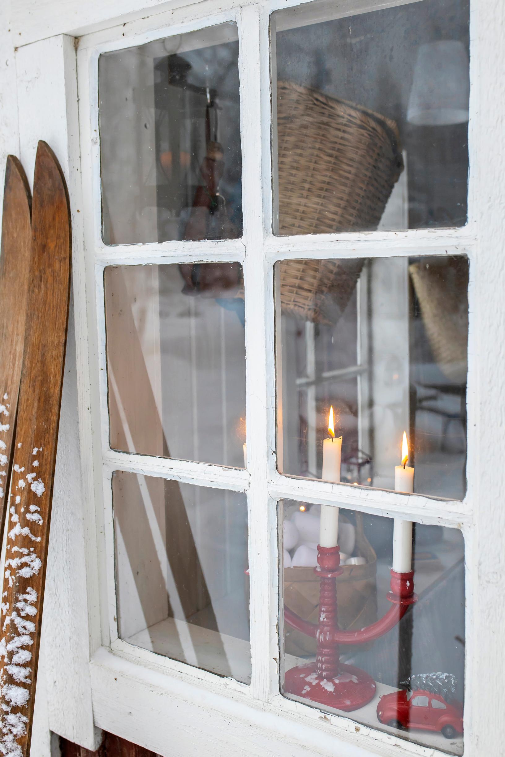 Old wooden skis on the wall, with a red candle holder visible through the window.