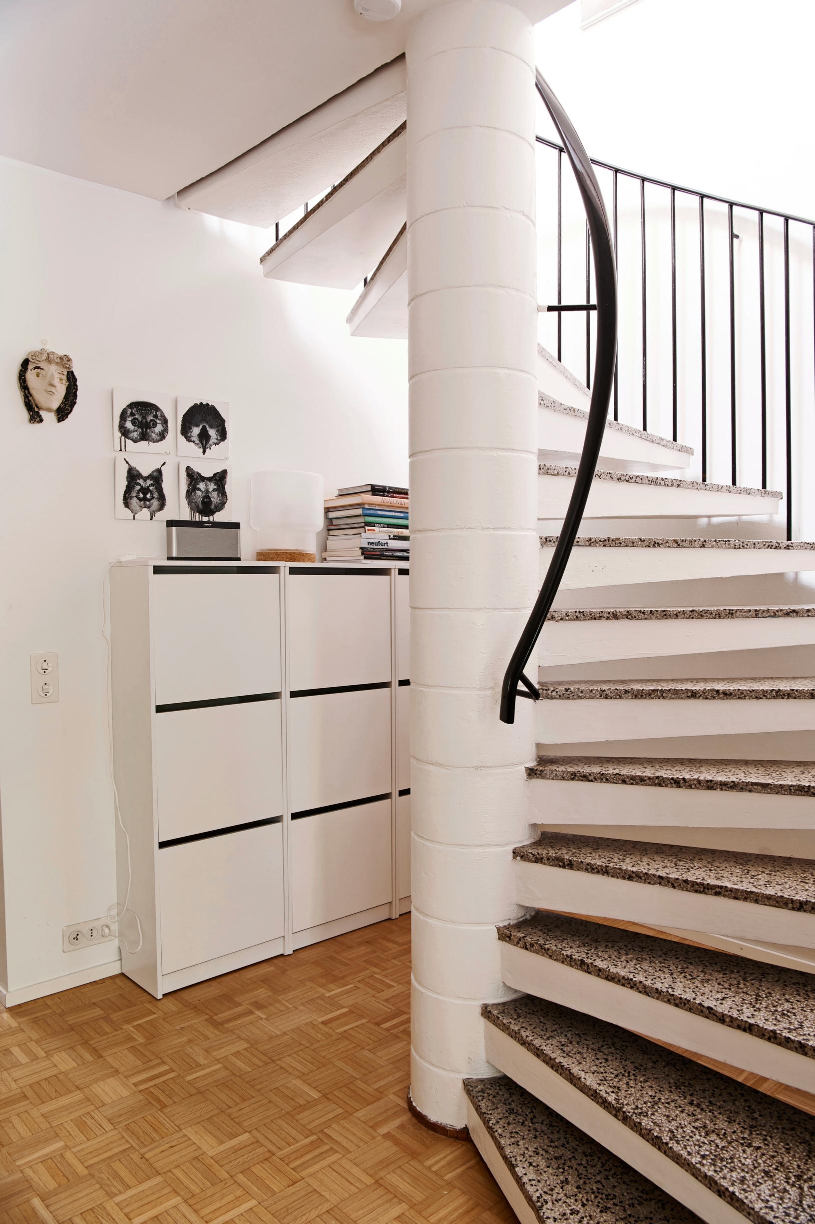 A white chest of drawers under a white spiral staircase