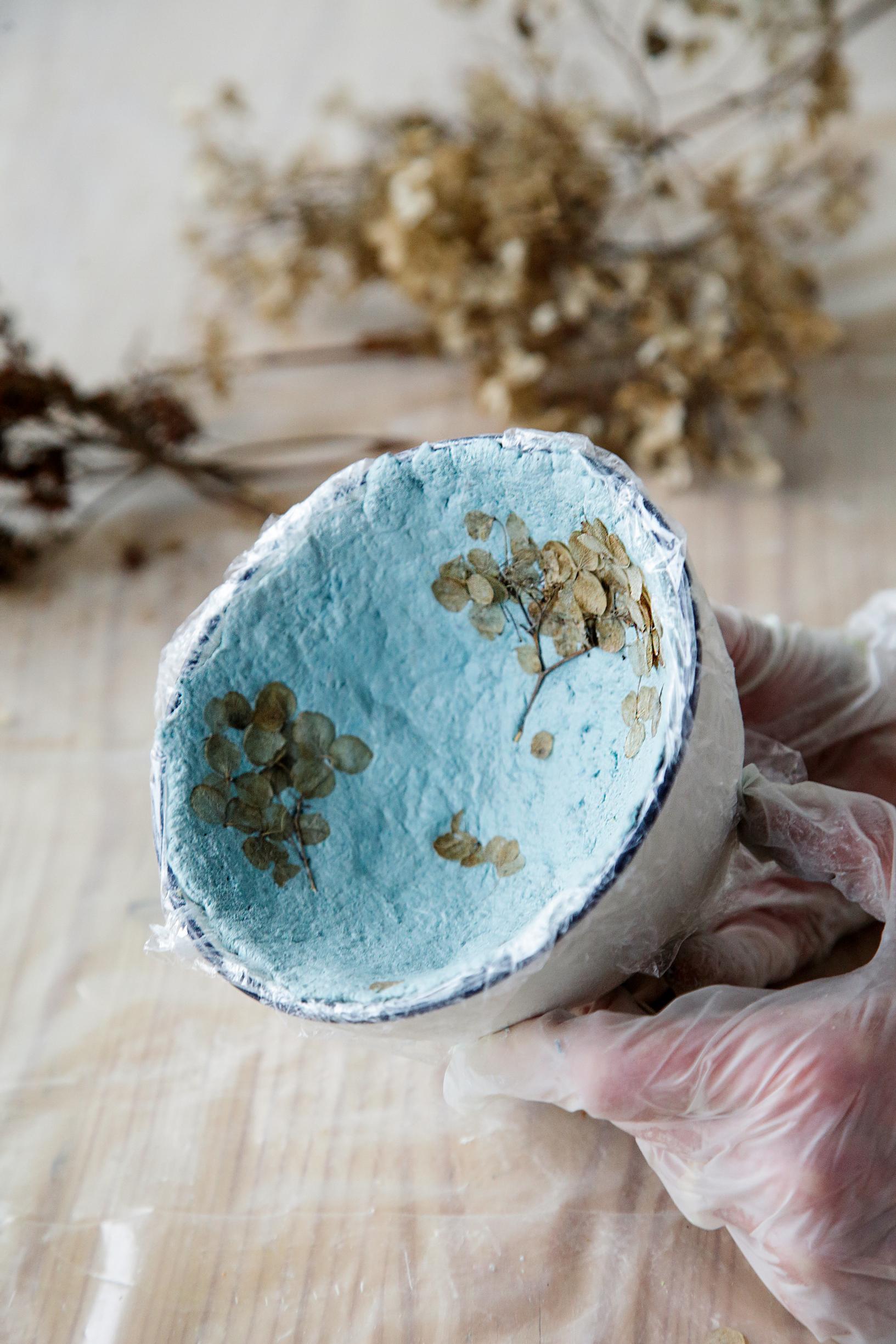 The inner surface of the papier-mâché bowl is decorated with a dried hydrangea flower.