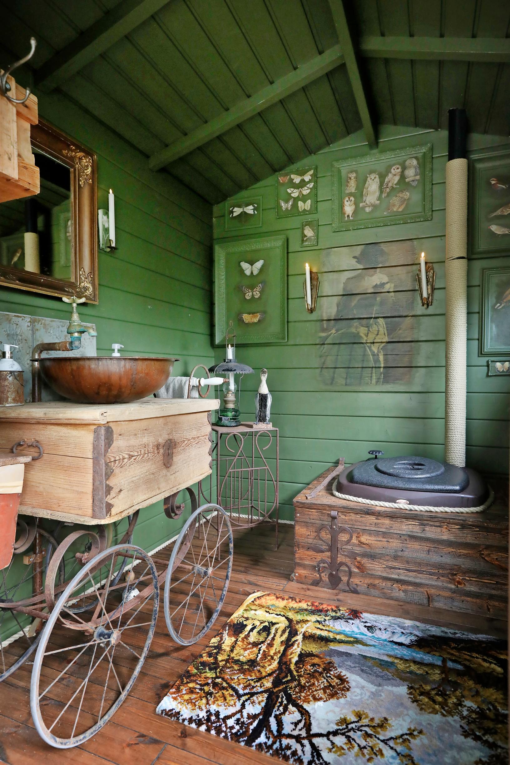 A green-walled outhouse, a sink counter made from a trunk with stroller wheels underneath, butterfly pictures on the wall.