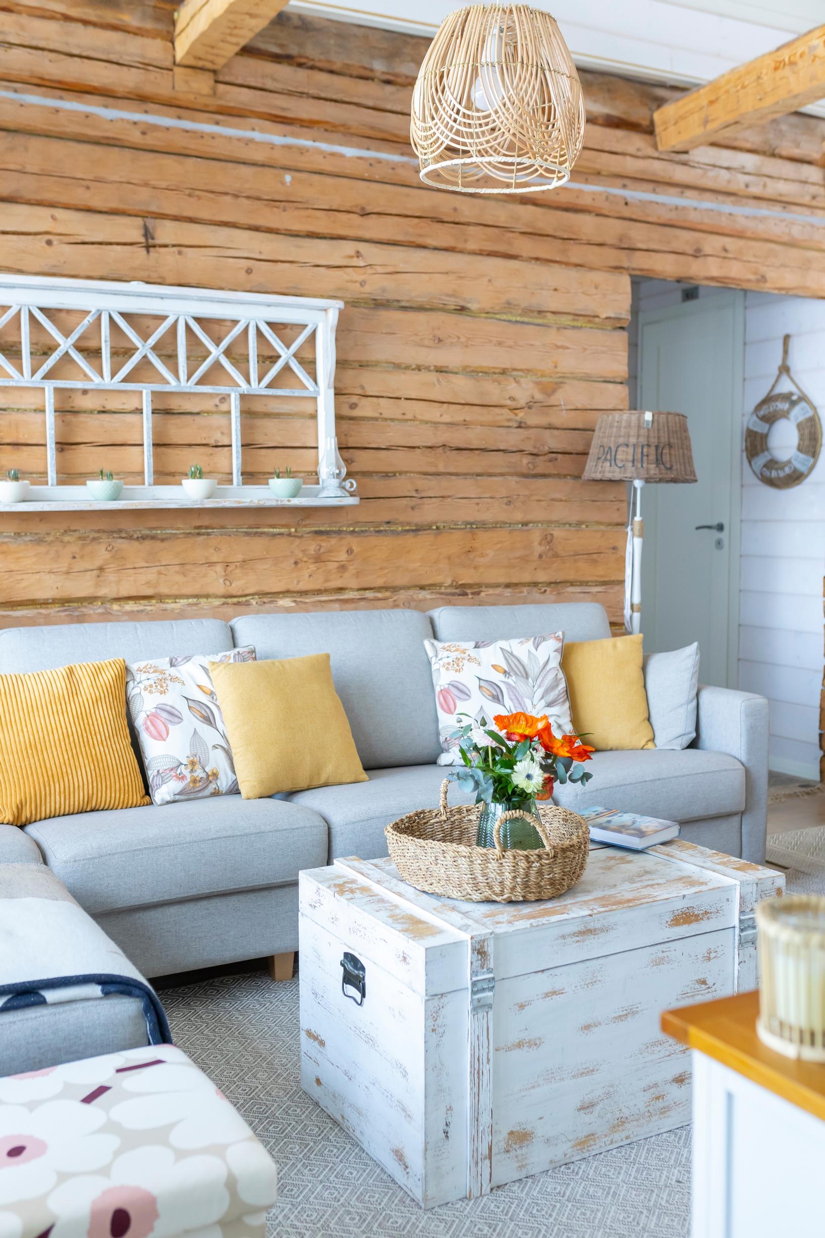 A log wall with a white shelf, a corner sofa with cushions, and a chest used as a coffee table