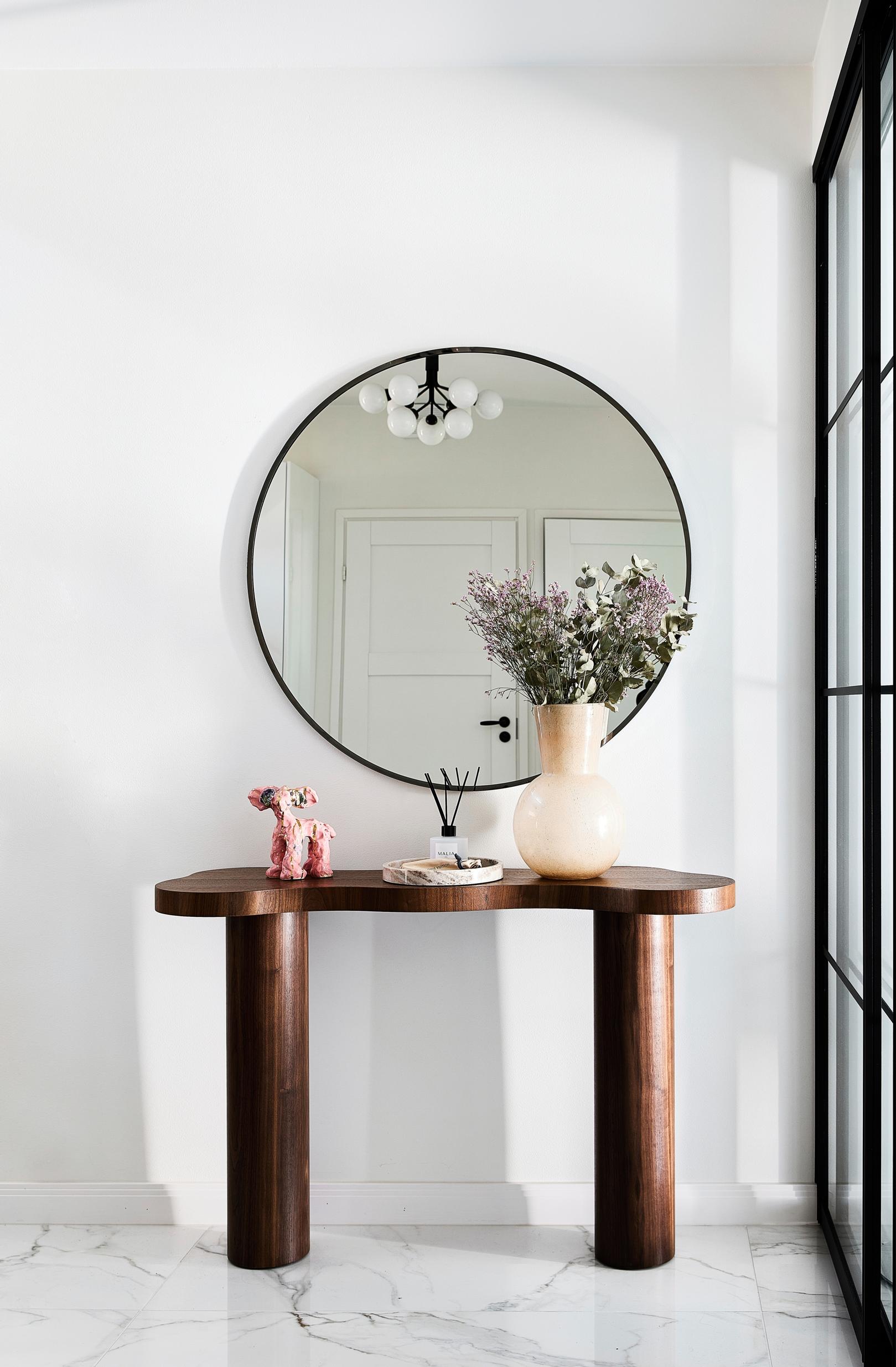 A side table and a round mirror in the hallway.