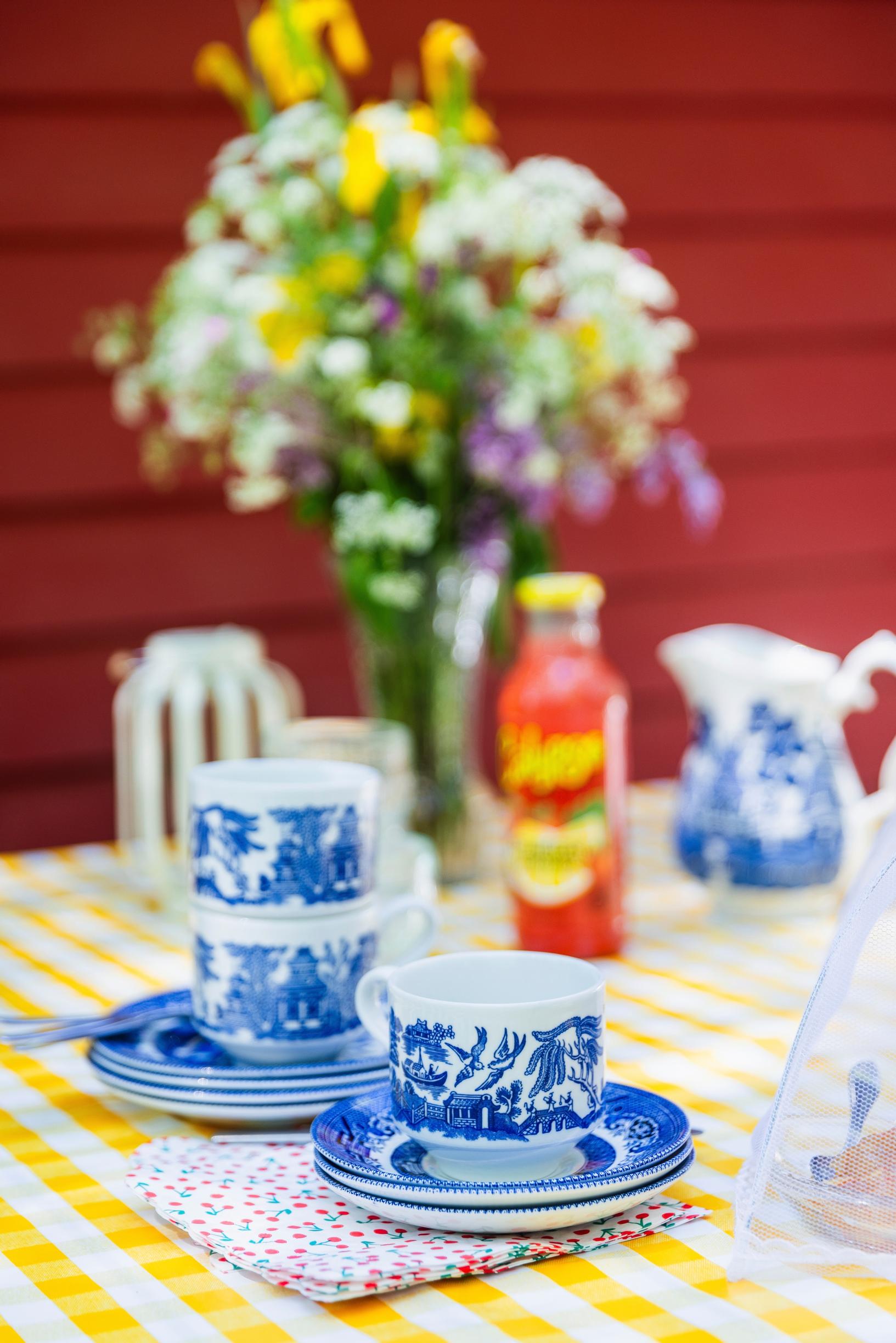 a stack of coffee cups and saucers on a garden table with a vase of flowers