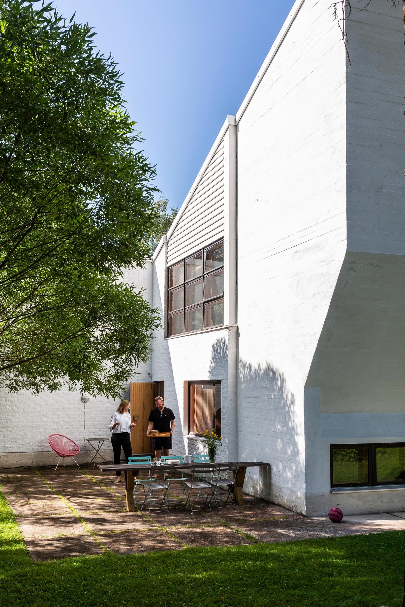 Exterior of the Alvar Aalto–designed heating plant in Rovaniemi, Eemil Karila and Heini-Tuuli Onnela outside, a tree and garden furniture